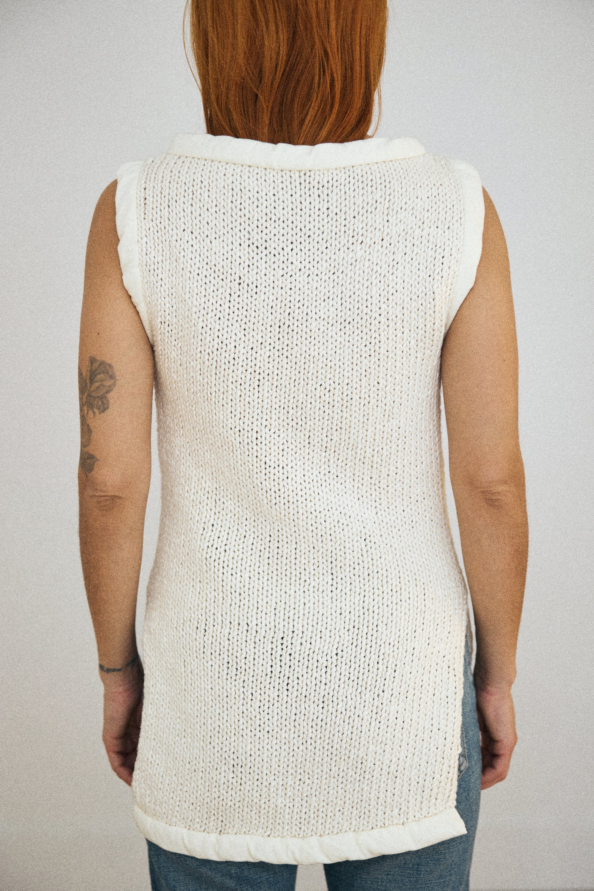 Person wearing a white knitted vest against a plain background