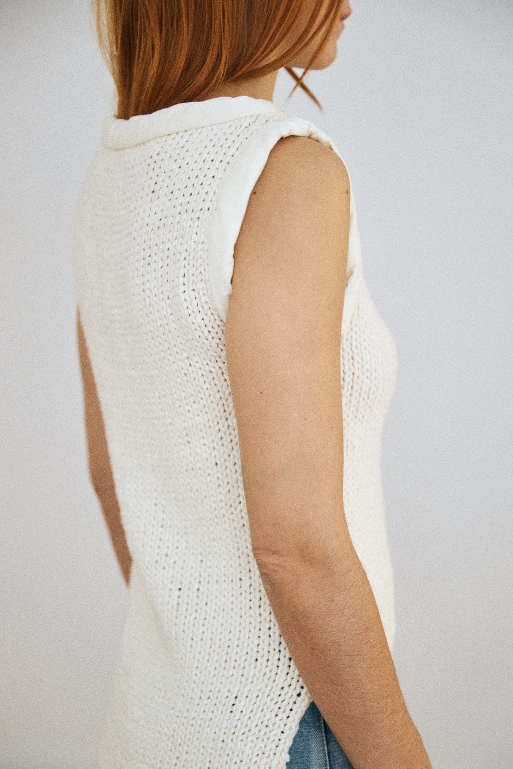 White sleeveless knitted top worn by a person on a plain background