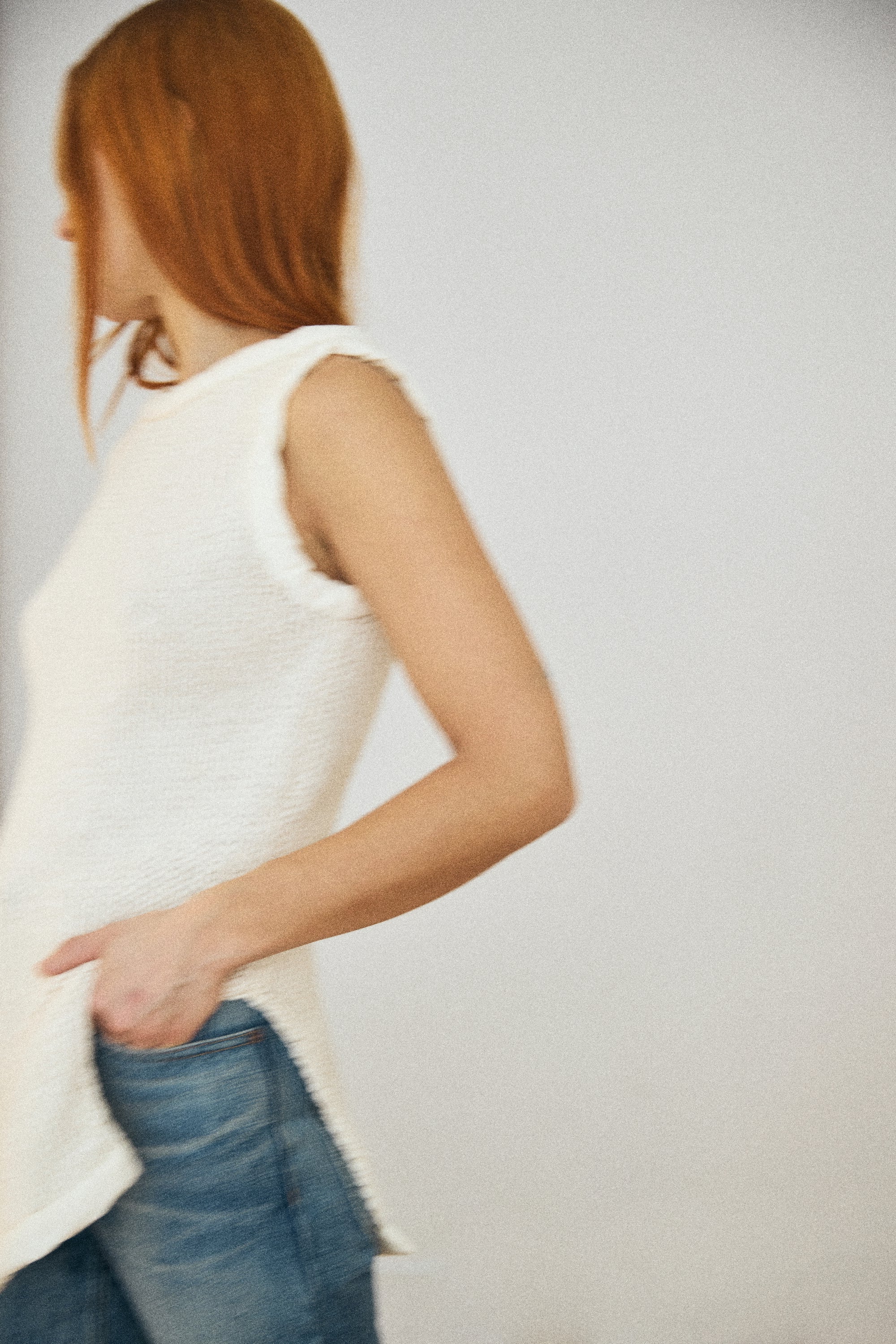 Person wearing a white sleeveless top and blue jeans against a plain background