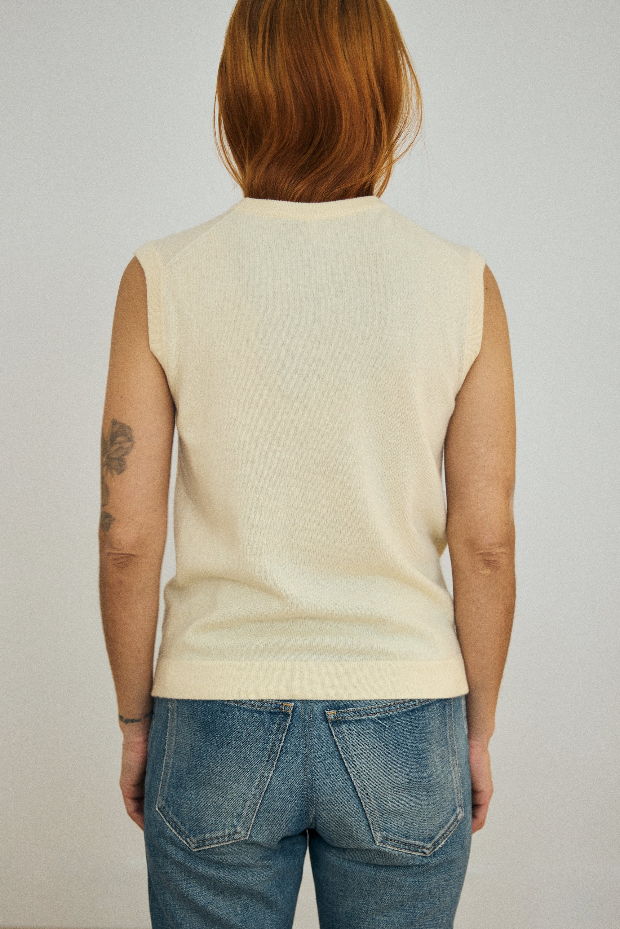 Person wearing a light-colored sleeveless top and blue jeans against a plain background