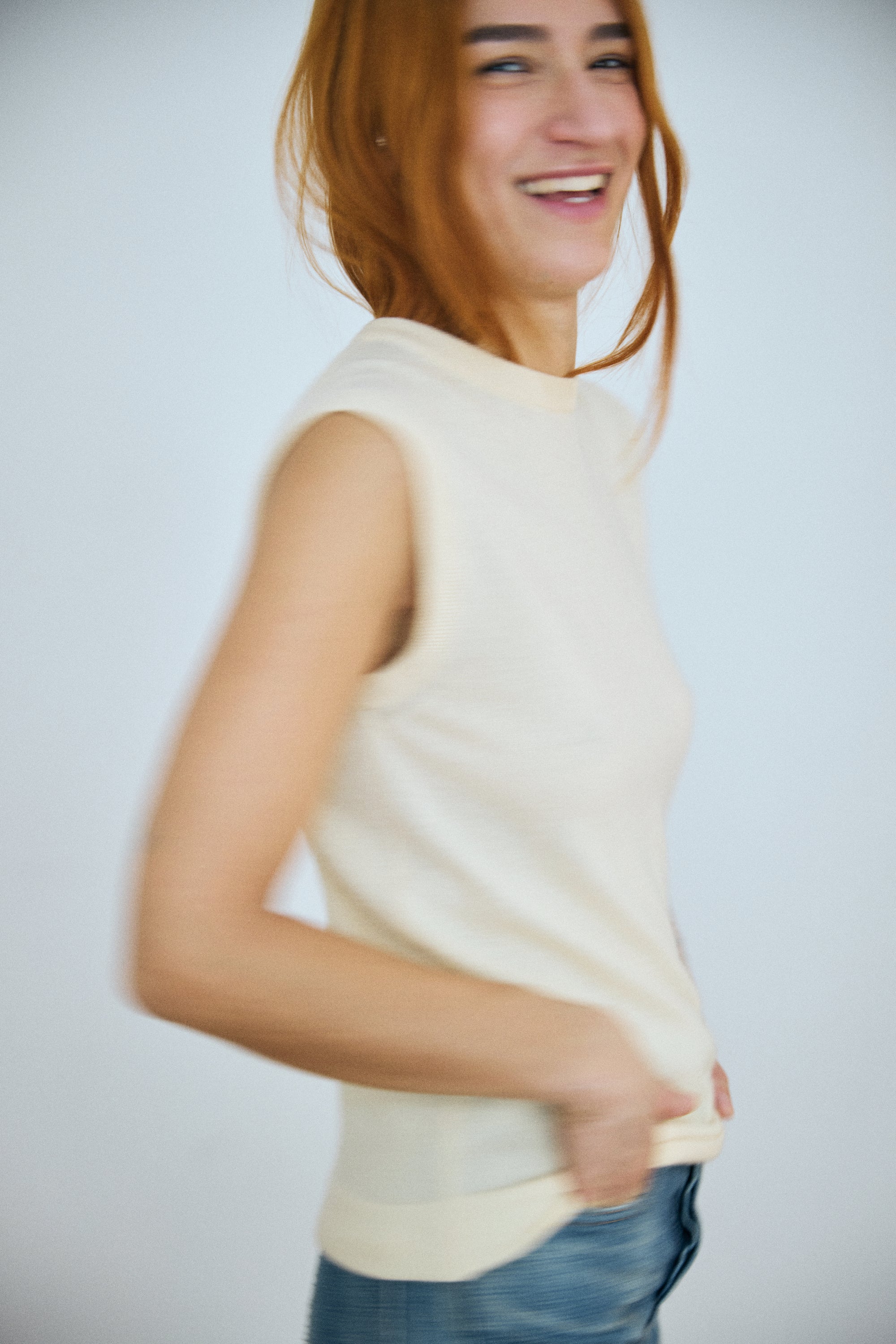Woman wearing a sleeveless cream top against a plain background