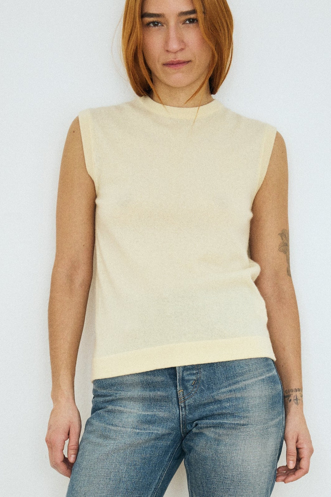 Person wearing a light-colored sleeveless top and blue jeans against a plain background