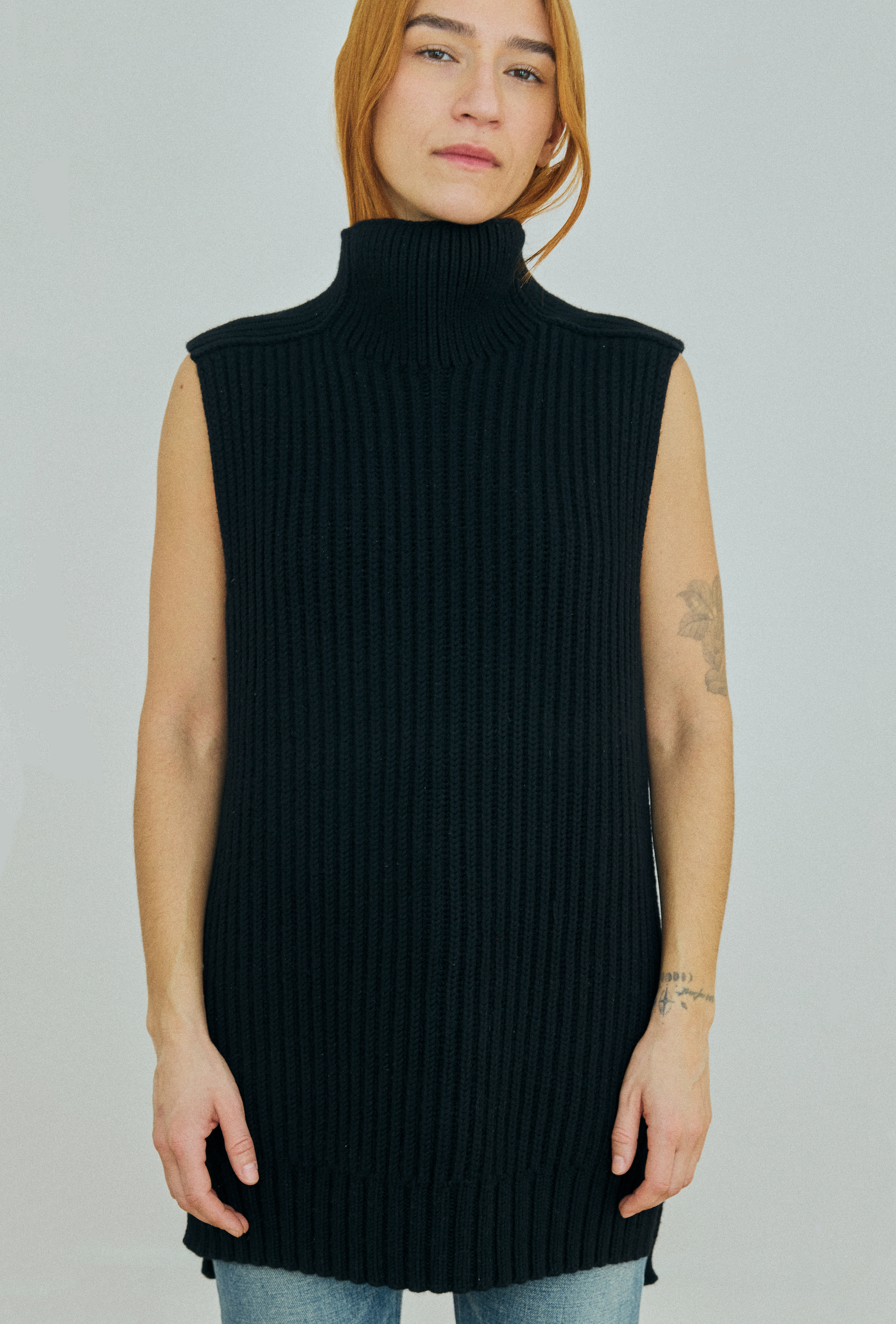 Person wearing a black sleeveless ribbed knit sweater on a plain background