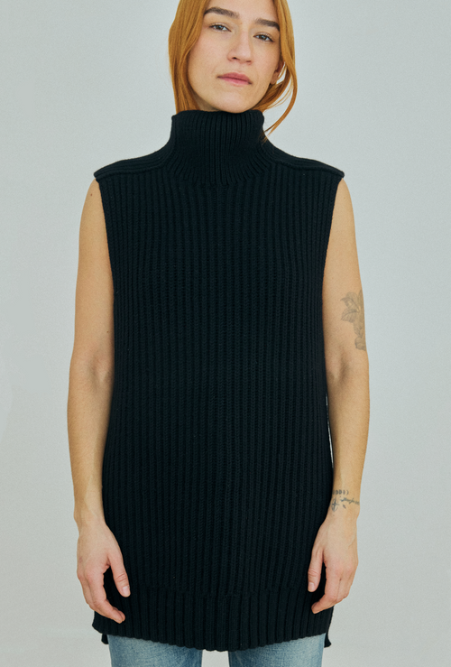 Person wearing a black sleeveless ribbed knit sweater on a plain background