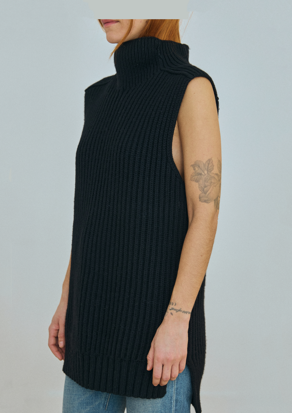 Person wearing a black sleeveless ribbed sweater against a plain background