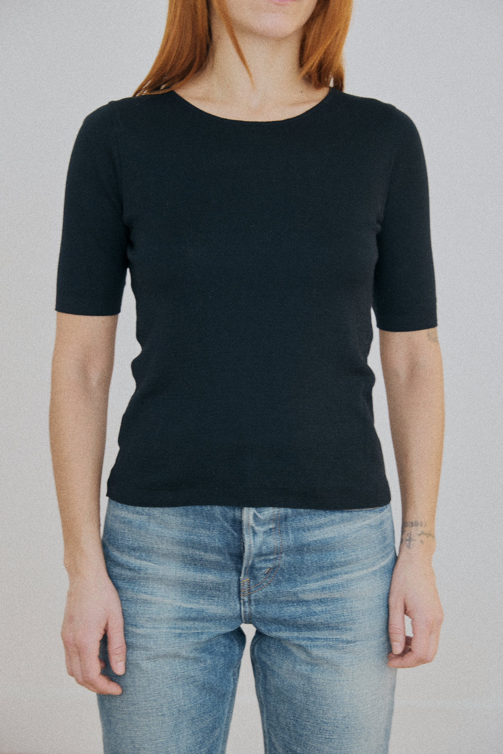 Person wearing a black short-sleeve shirt and blue jeans against a plain background