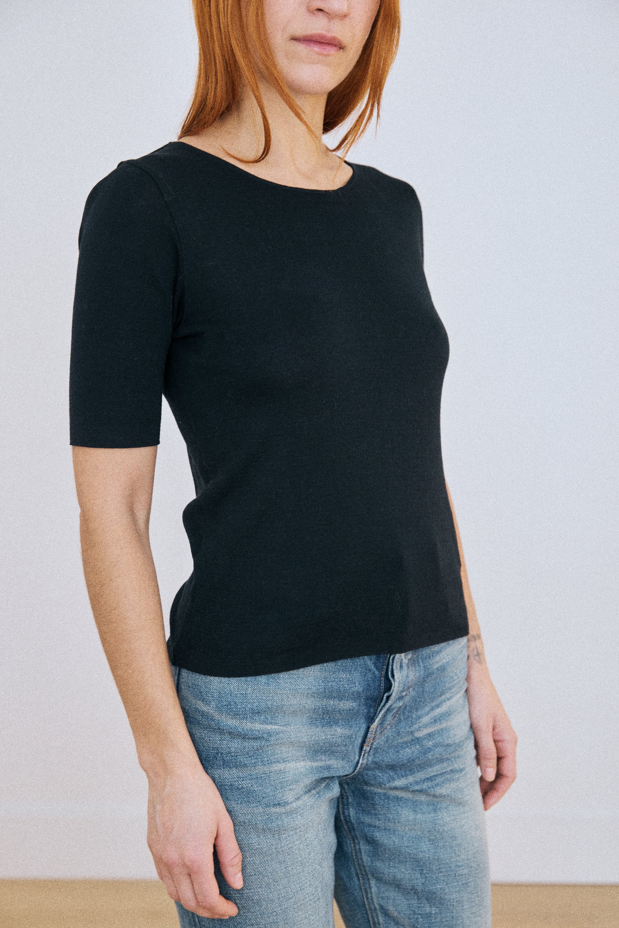 Person wearing a black top and blue jeans against a plain background