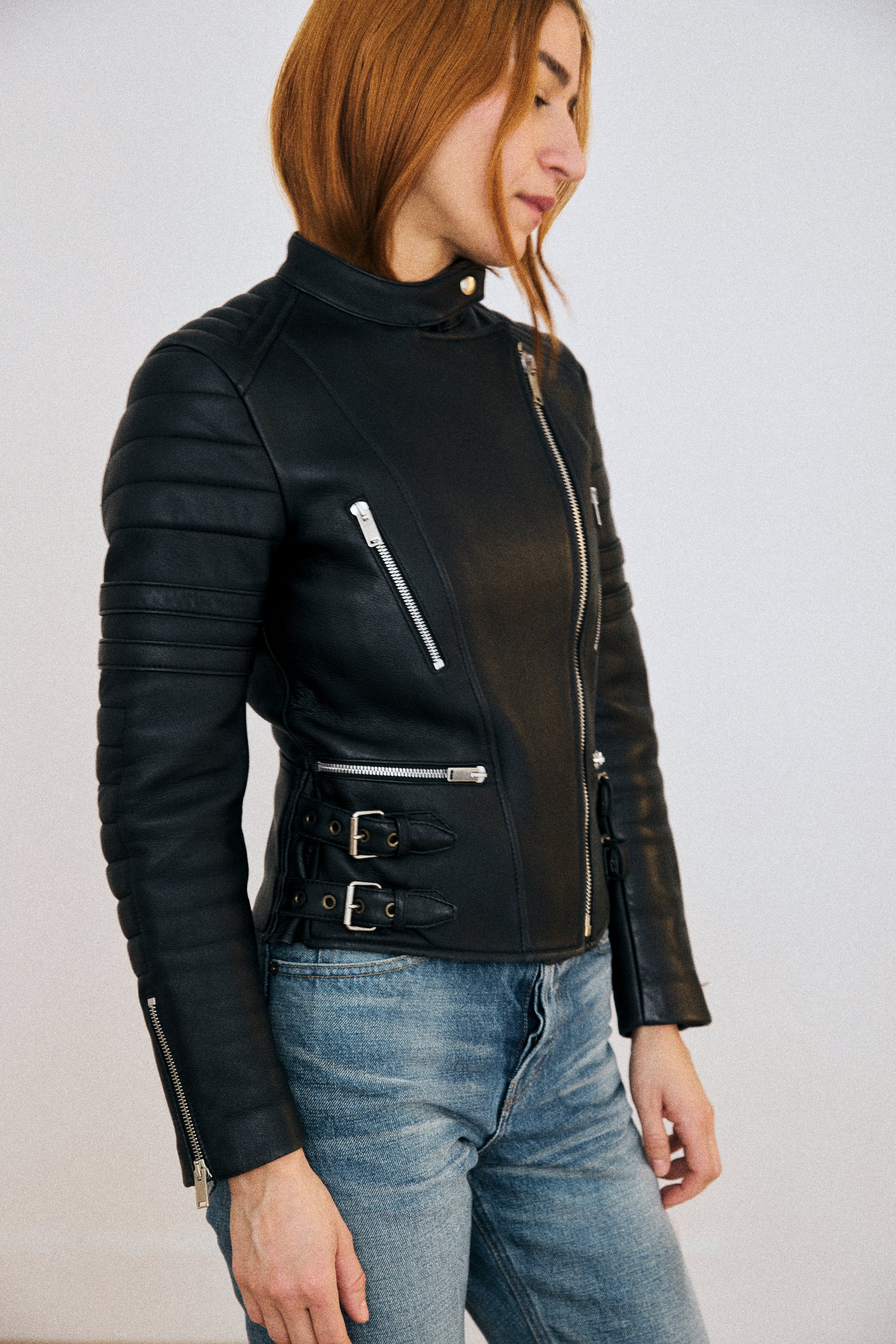 Person wearing a black leather jacket with silver zippers on a plain background