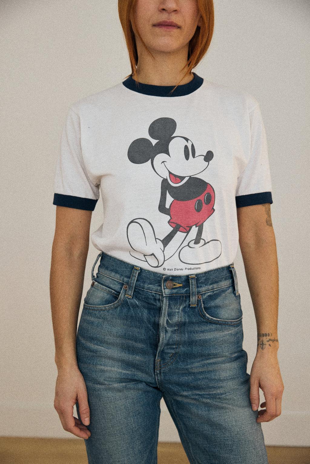 Person wearing a t-shirt with a cartoon character design and blue jeans against a plain background