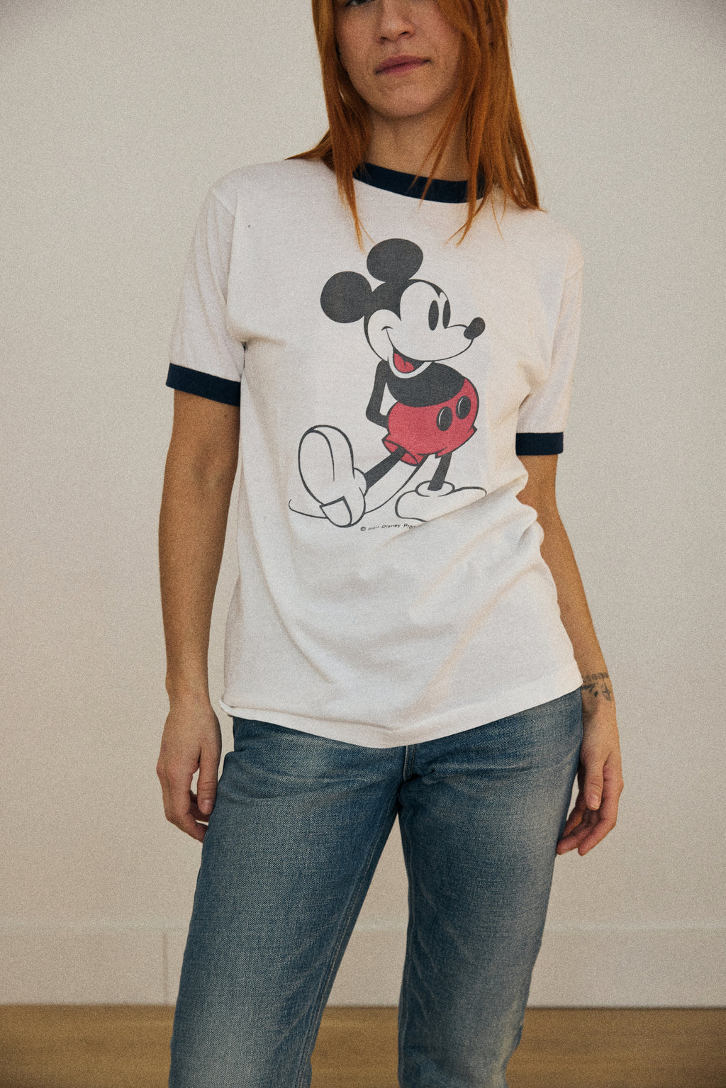 Person wearing a white t-shirt with a cartoon character design and blue jeans against a plain background