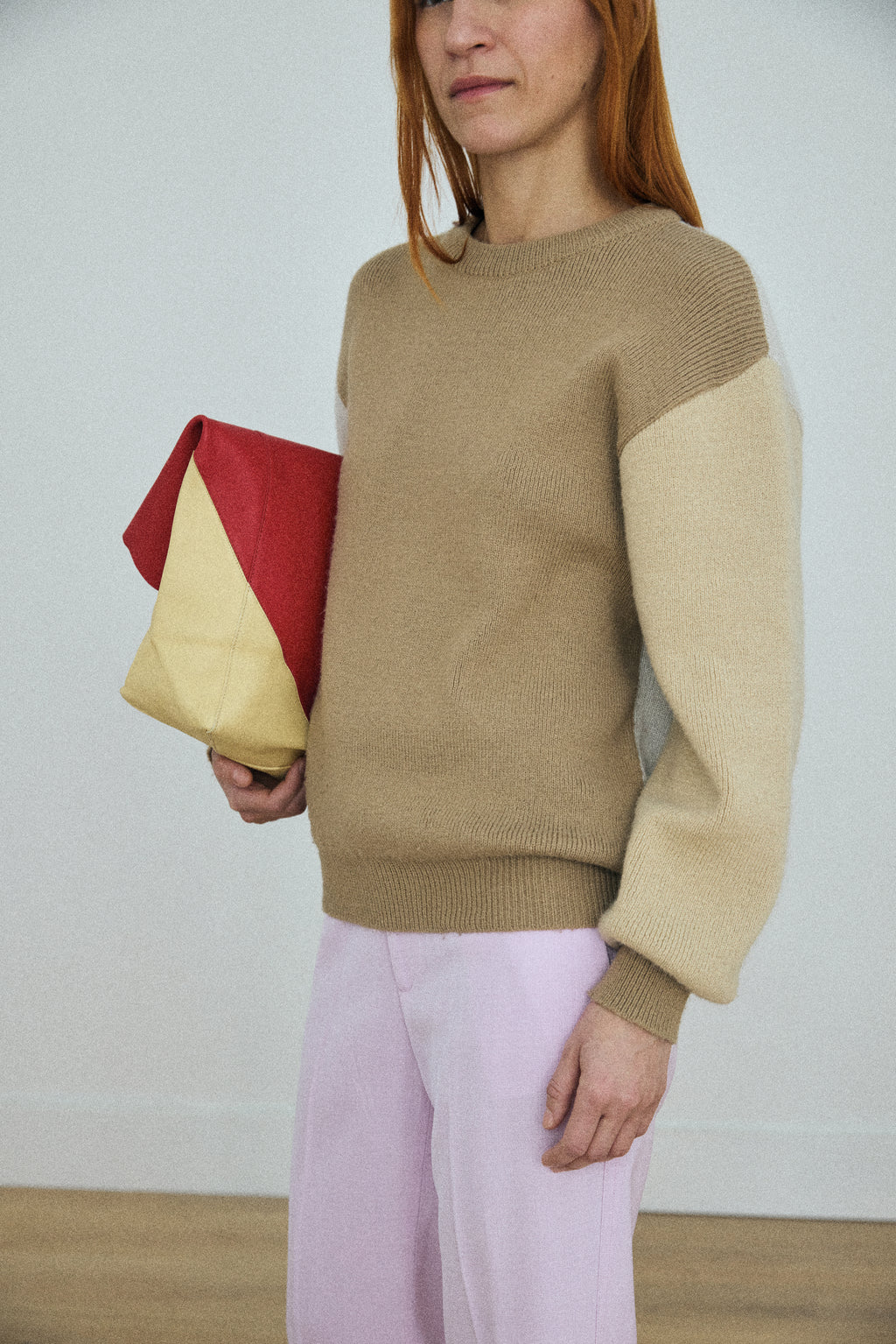 Woman wearing a beige sweater holding a colorful clutch against a plain background