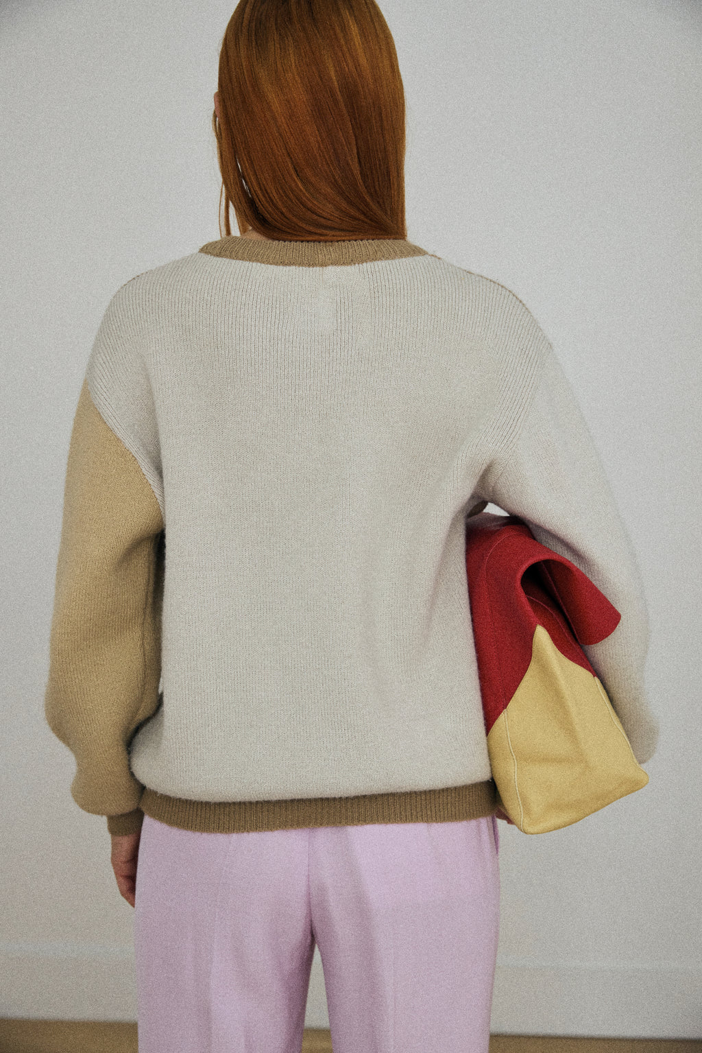 Person wearing a color-blocked sweater with beige, red, and yellow sections.