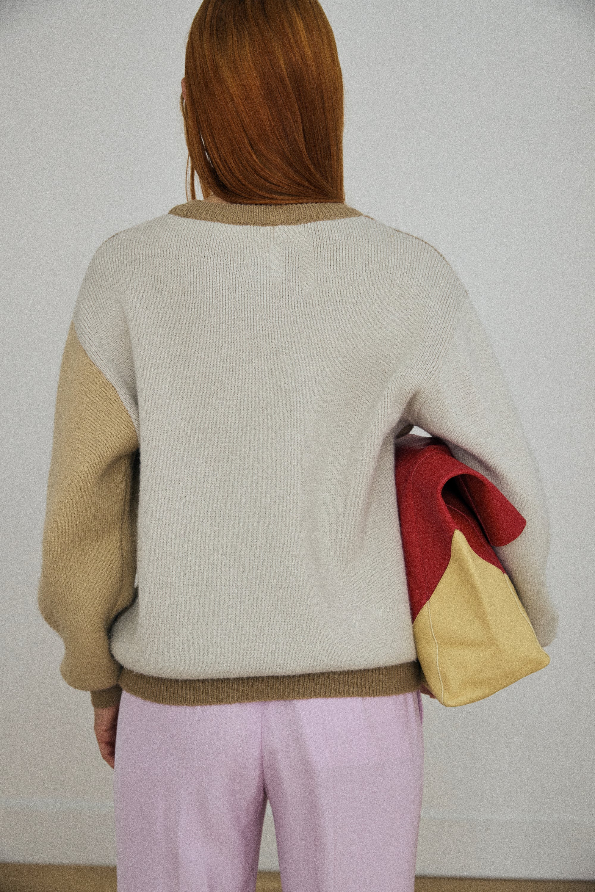 Person wearing a color-blocked sweater with beige, red, and yellow sections.