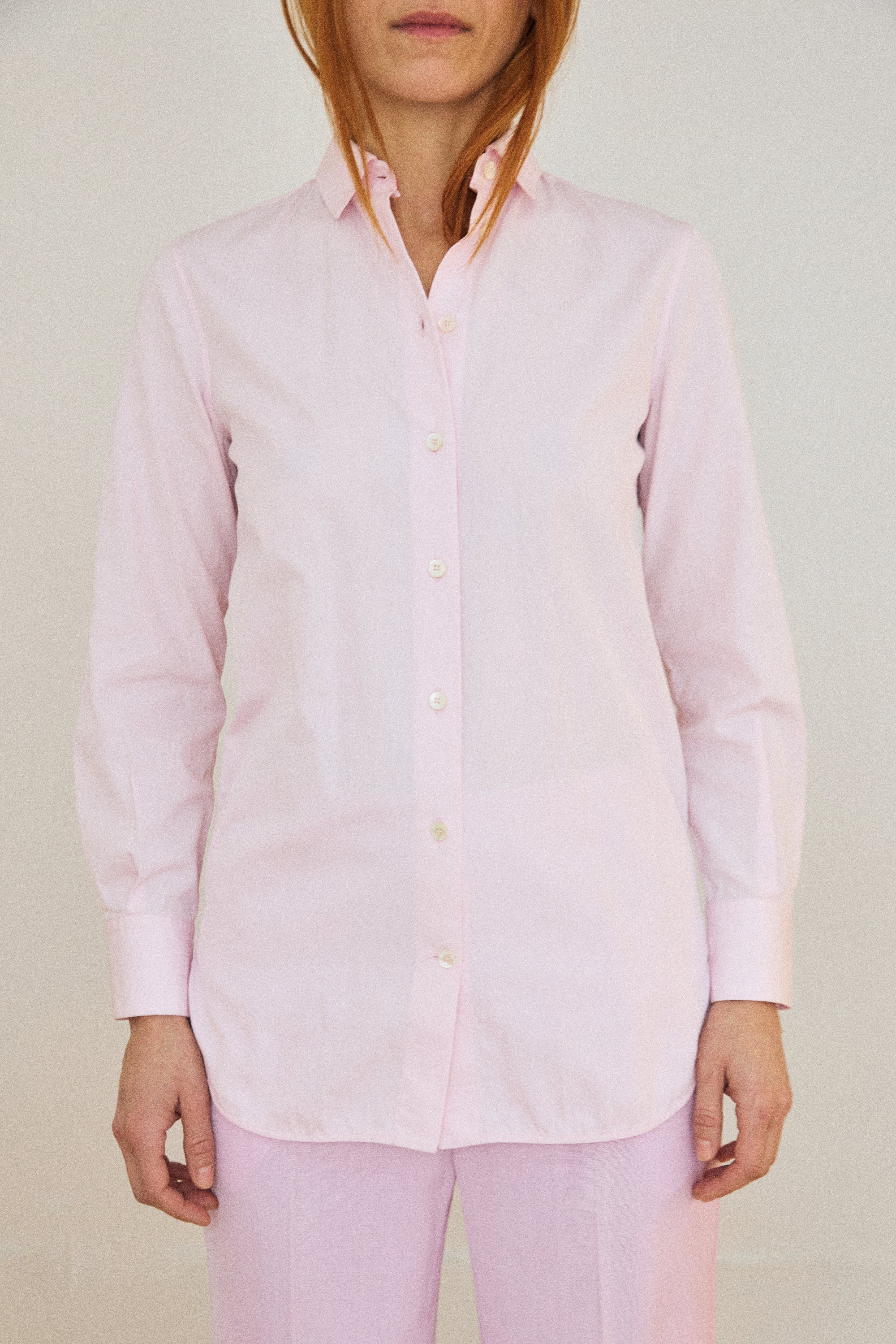 Person wearing a light pink button-up shirt and pants against a plain background