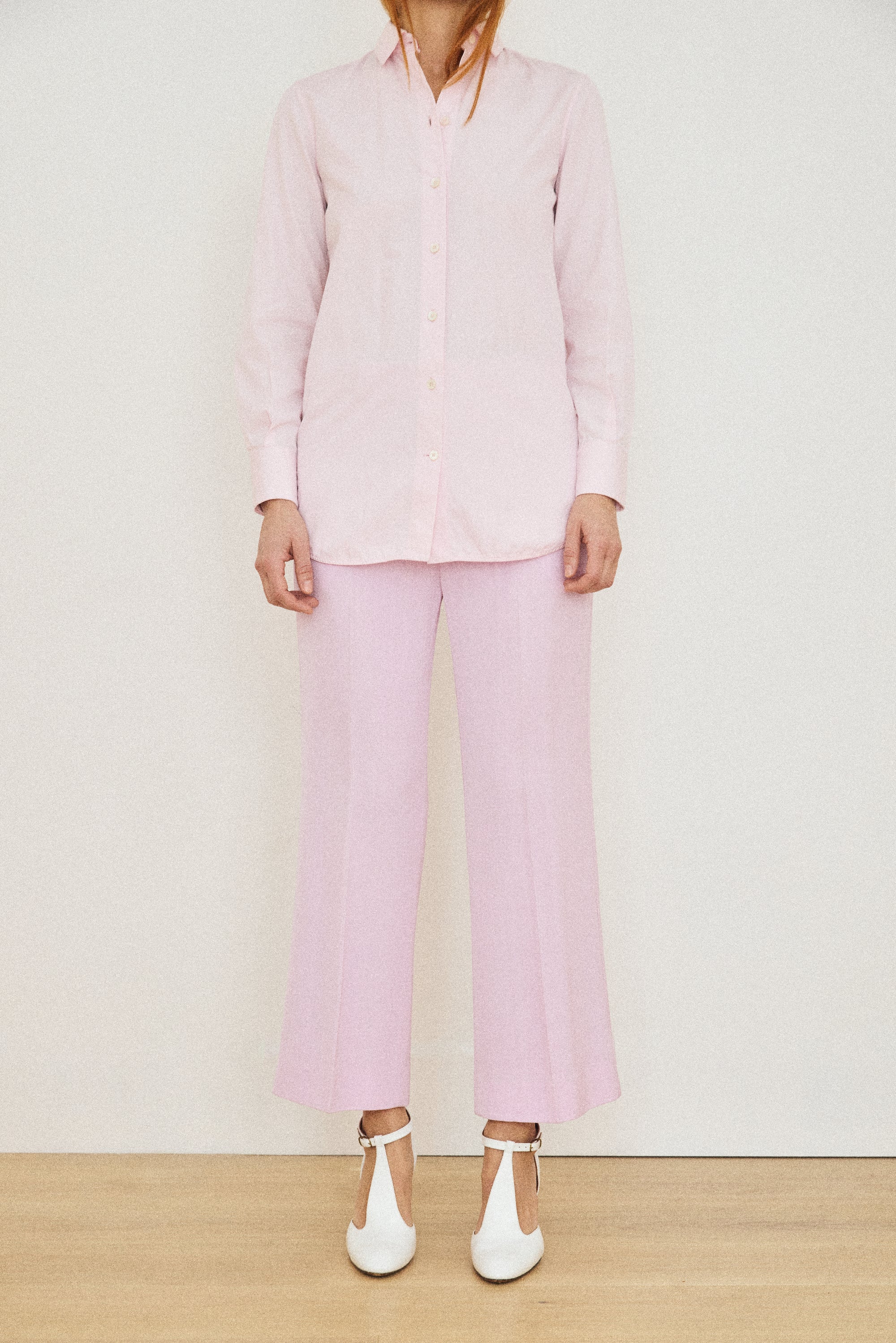 Person wearing a light pink outfit with a shirt and pants, standing against a white background.