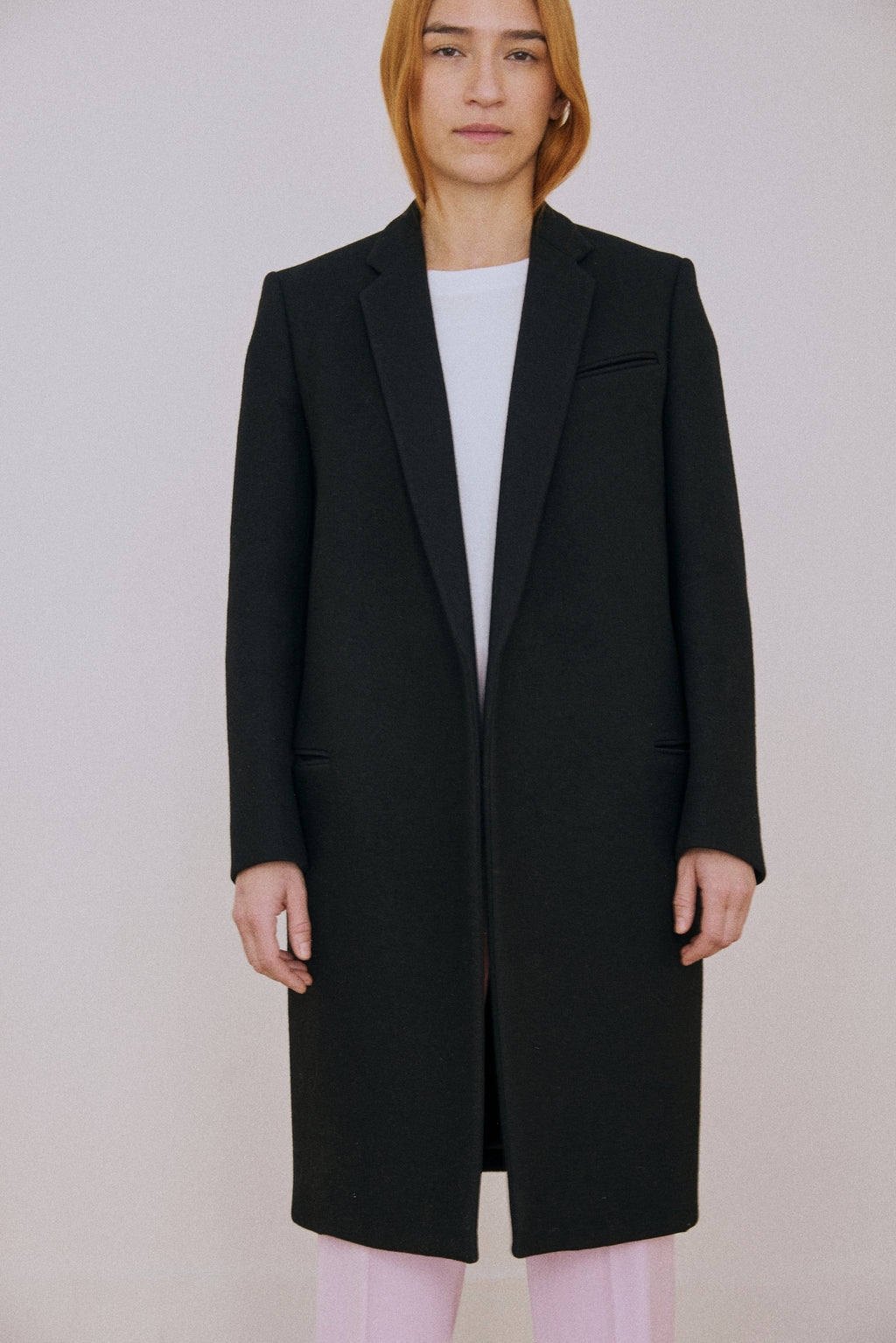 Person wearing a black coat against a plain background