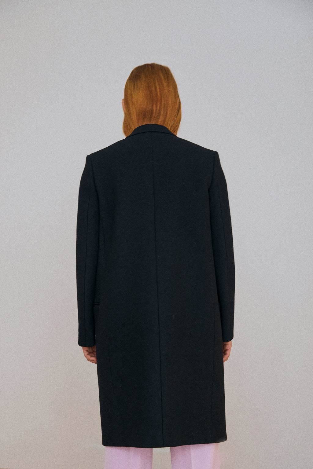 Person wearing a black coat from behind on a plain background