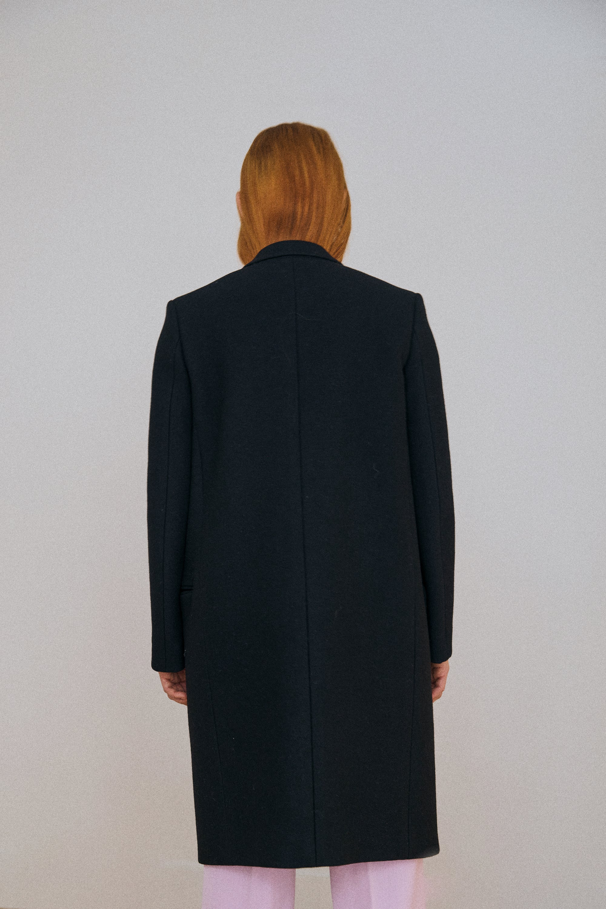 Person wearing a black coat from behind on a plain background