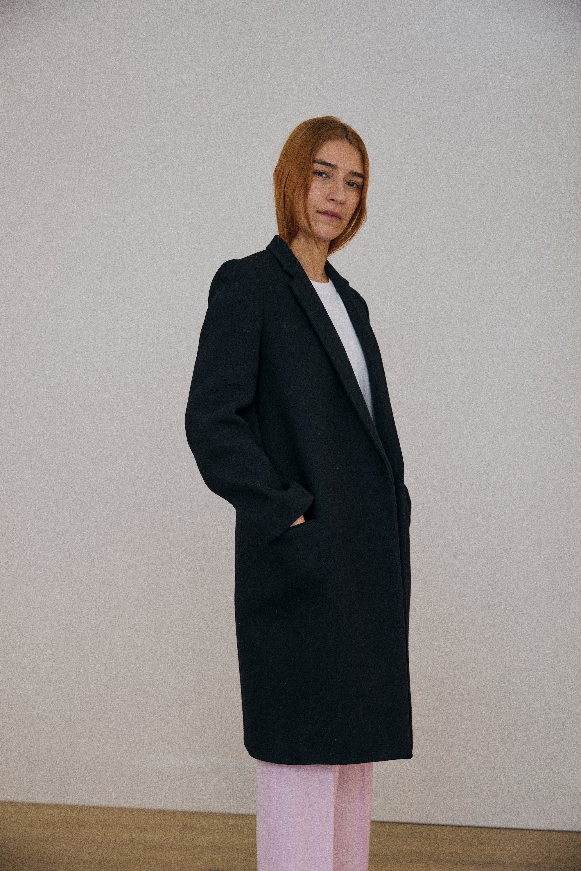 Person wearing a black coat against a plain background