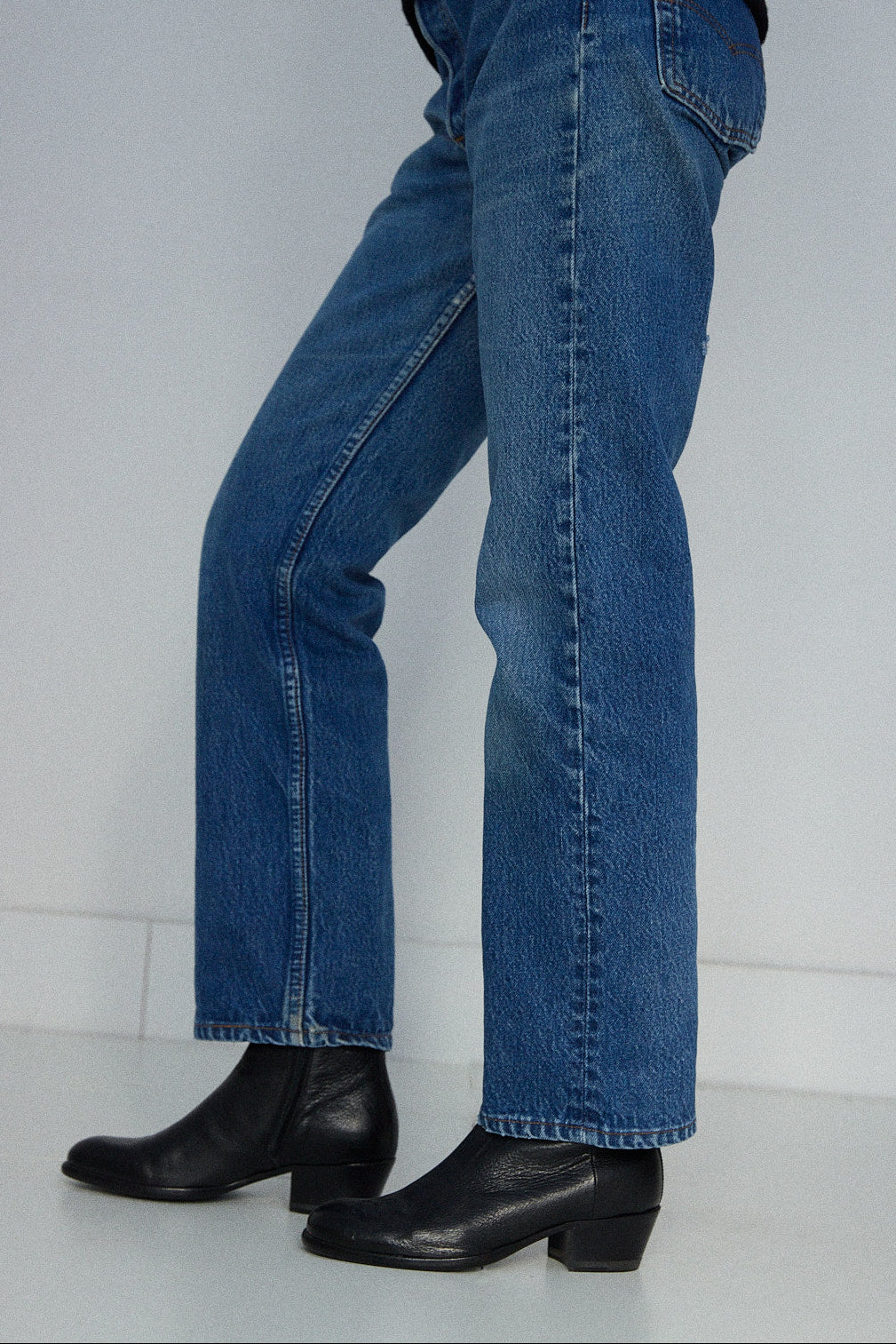 Person wearing blue jeans and black boots on a white background