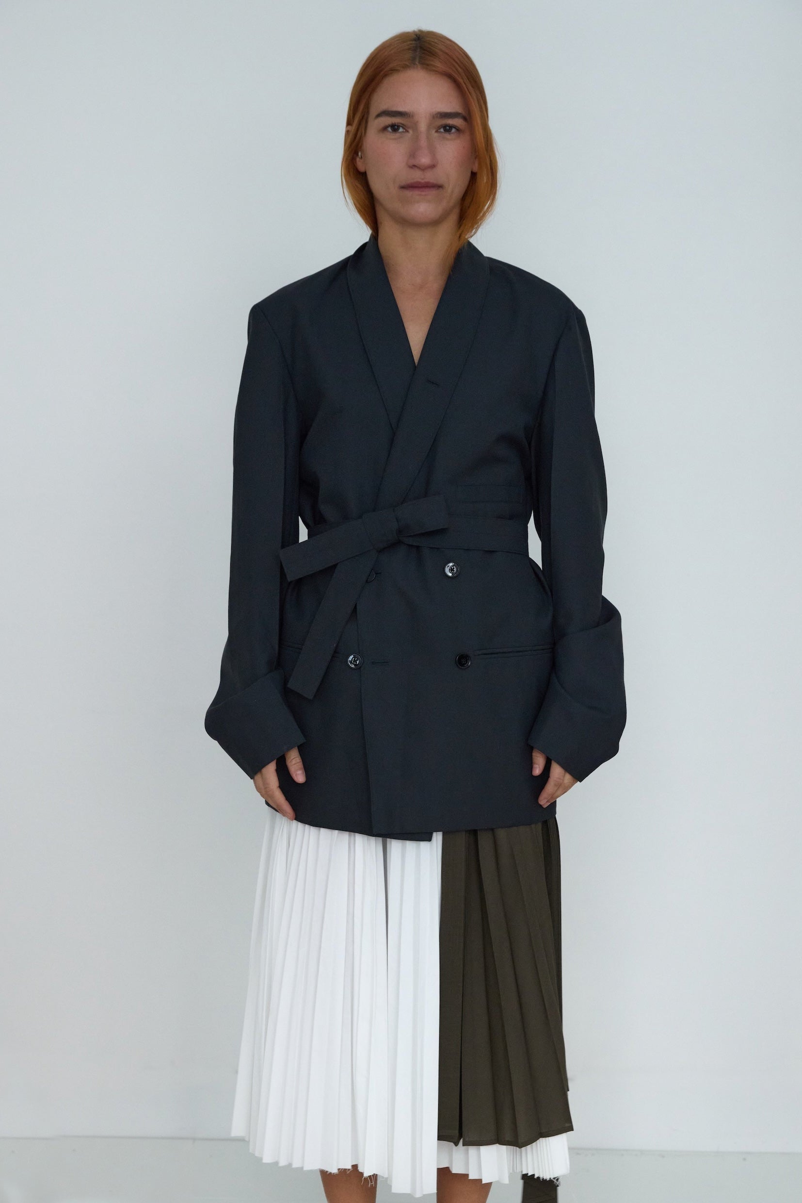 Person wearing a black coat with a white and green skirt on a plain background