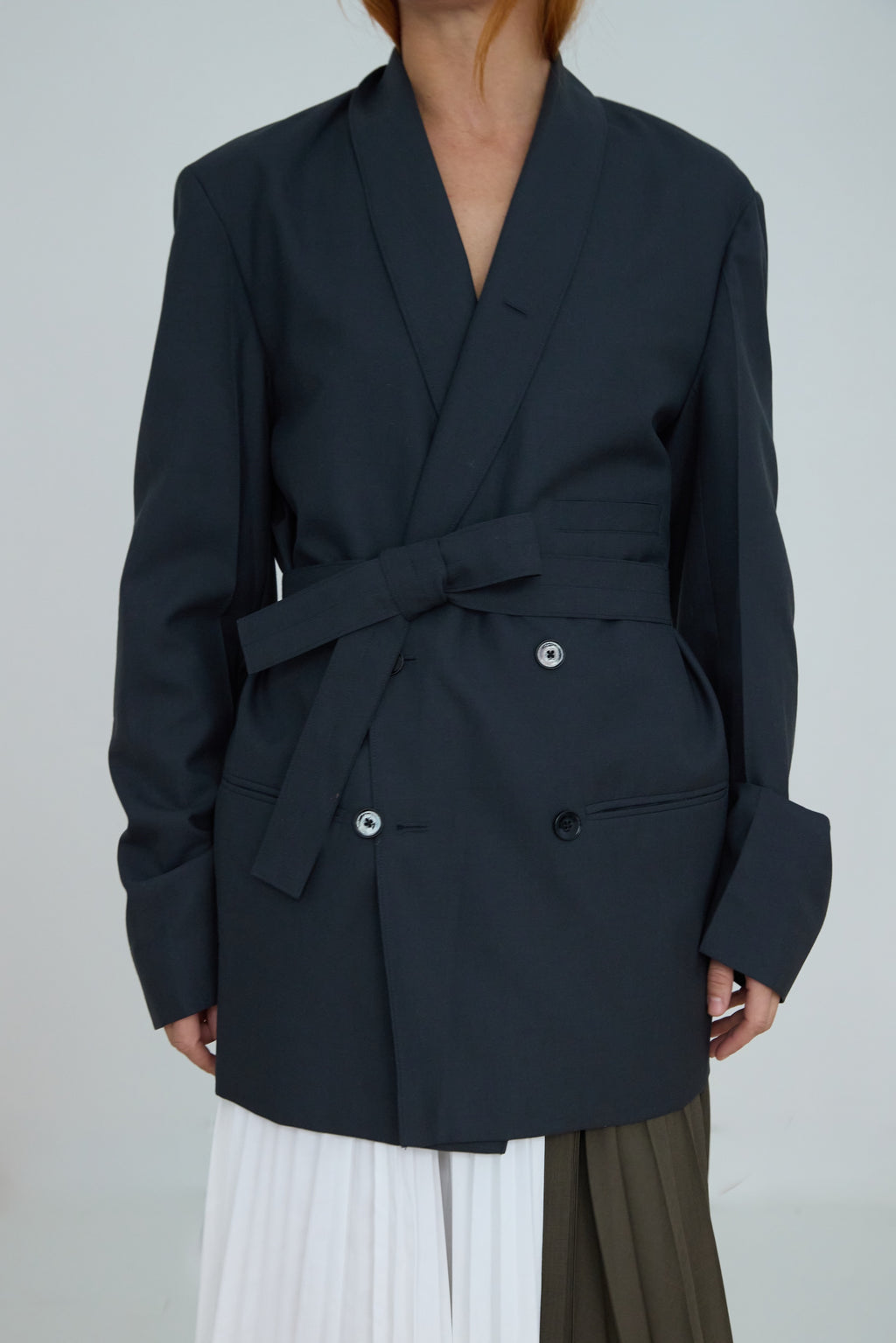 Person wearing a dark blue blazer with a belt on a plain background