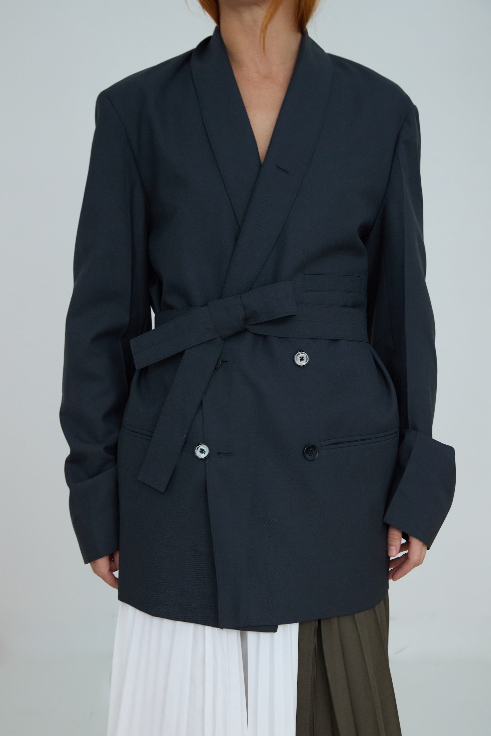 Person wearing a dark blue blazer with a belt on a plain background