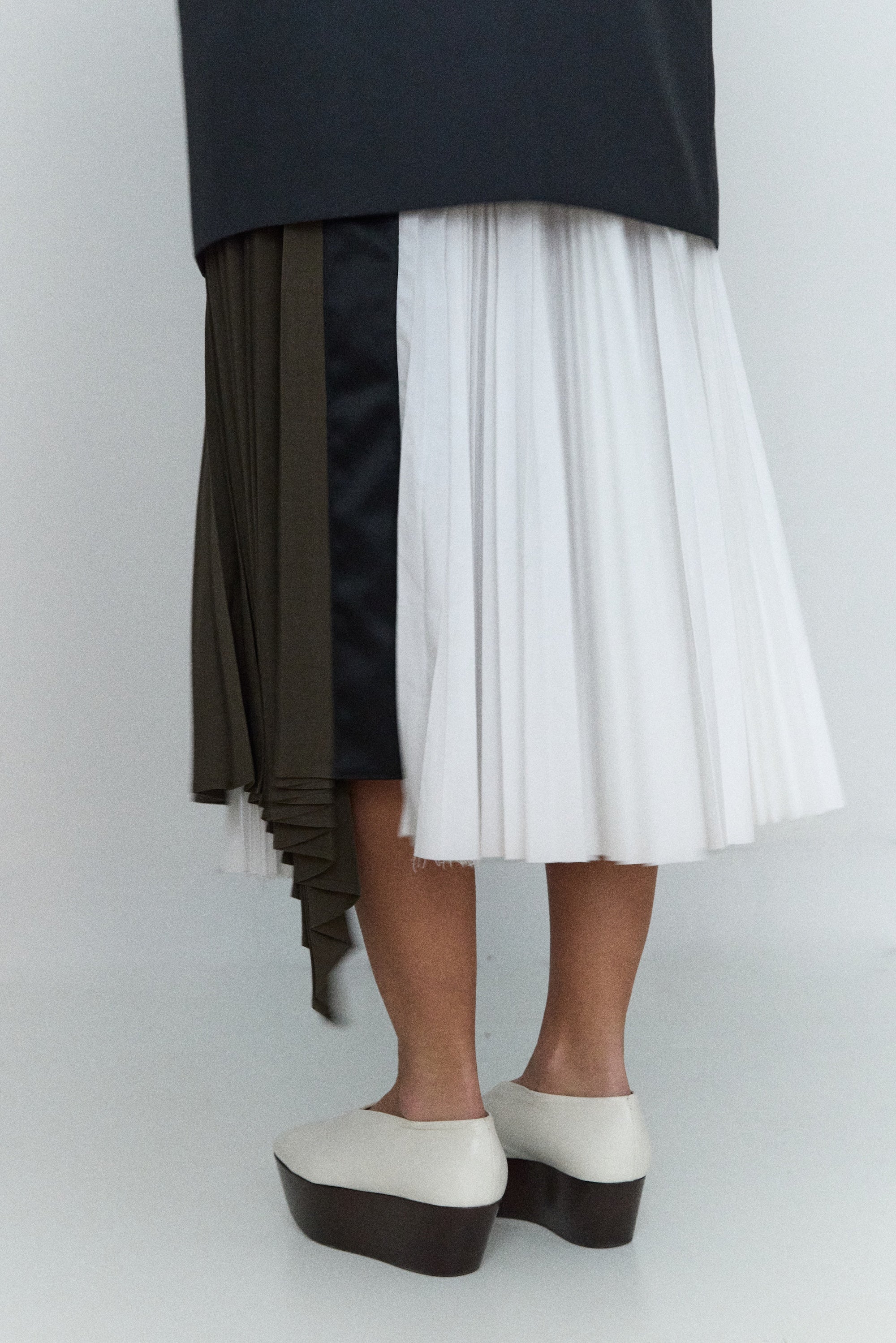 Person wearing a black top and a pleated skirt with color-blocked design on a white background