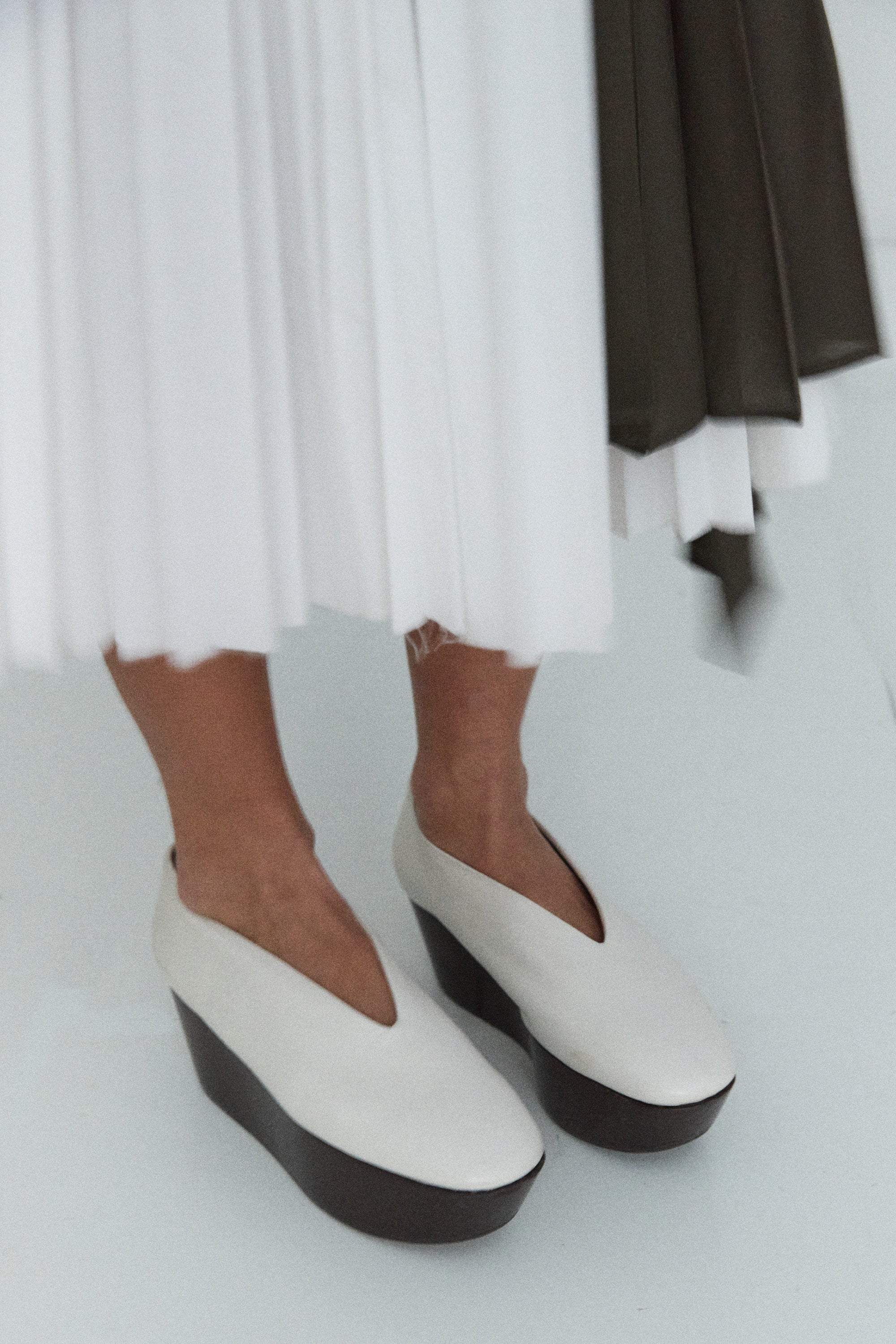 White platform shoes worn with a white skirt on a light gray background