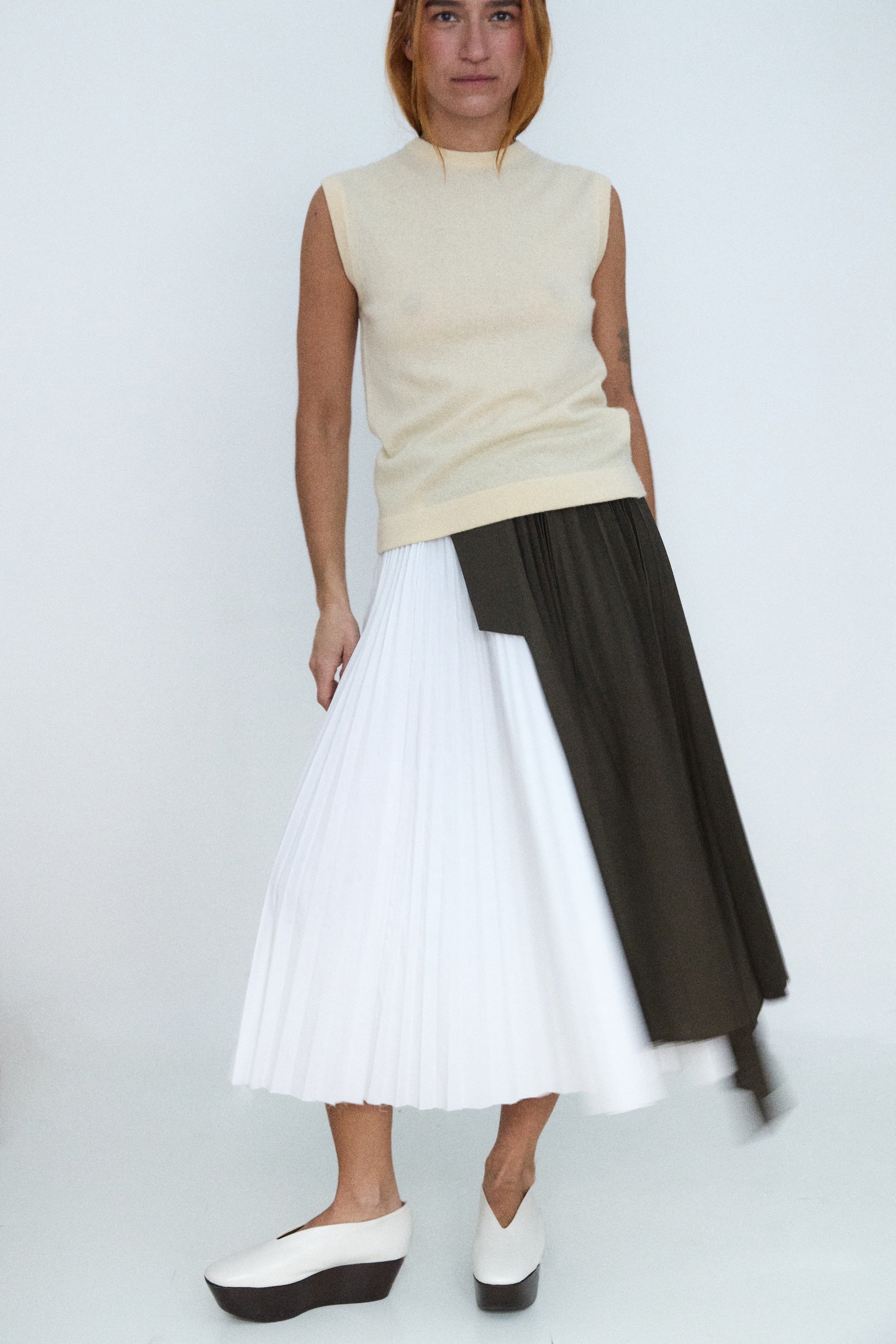 Person wearing a sleeveless beige top and a two-tone skirt with white and black colors on a plain background.