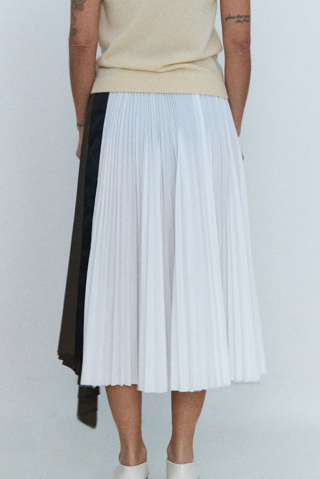 Person wearing a beige top and pleated skirt with a white background