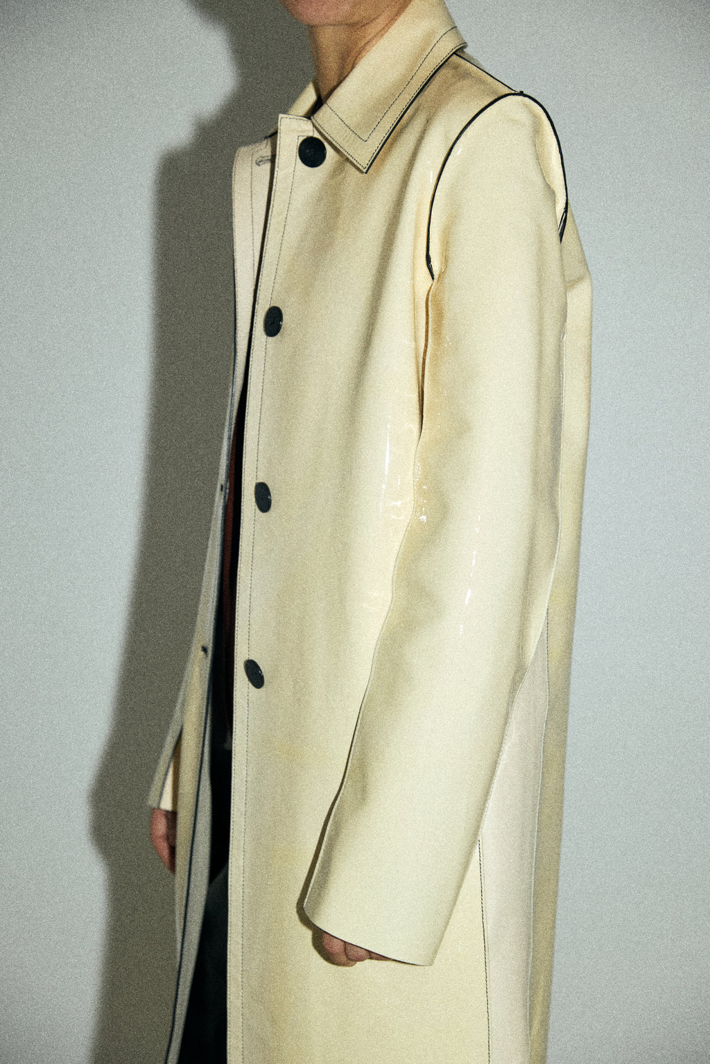 Beige trench coat with black buttons on a plain background