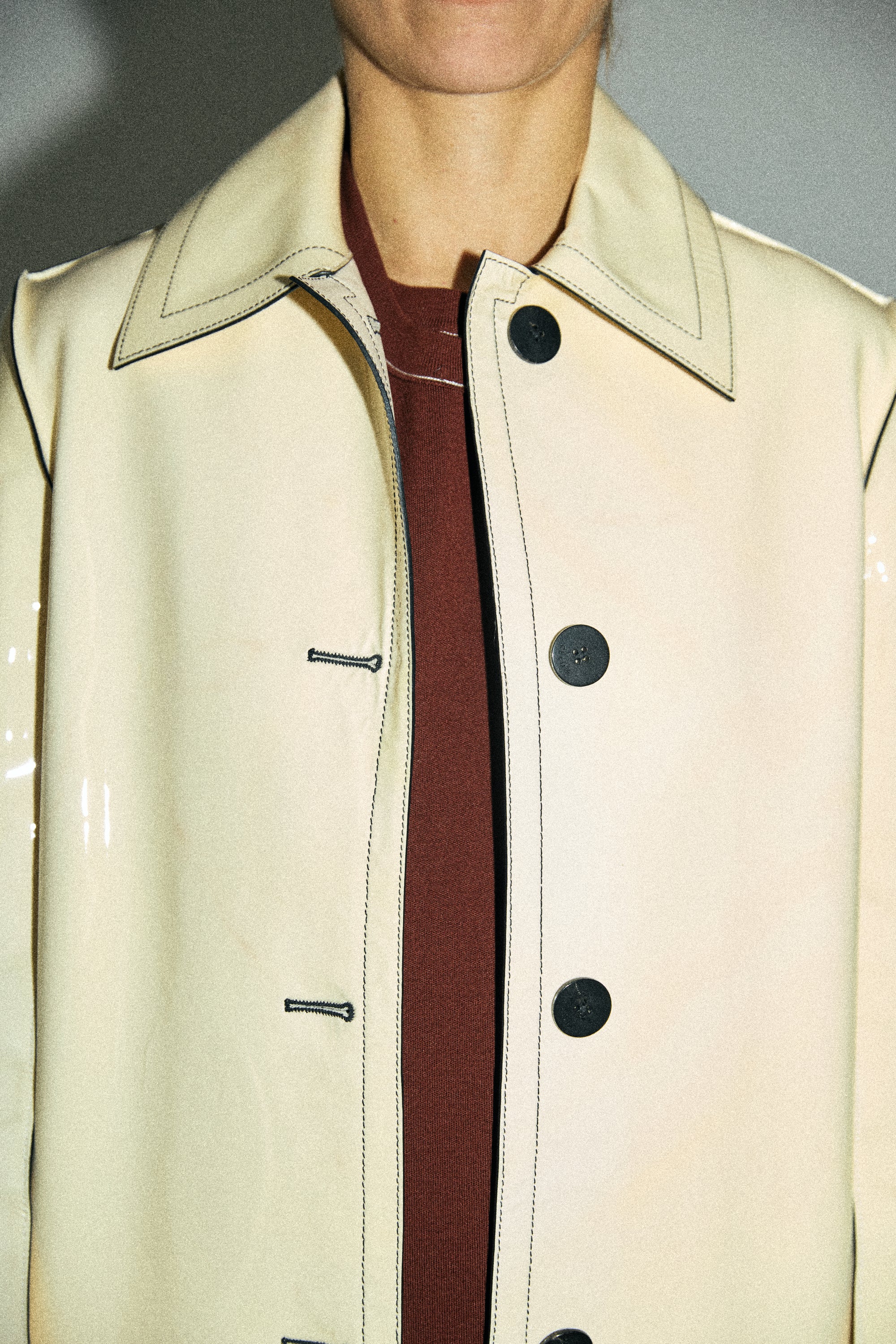 Close-up of a beige trench coat with a zipper and buttons on a neutral background