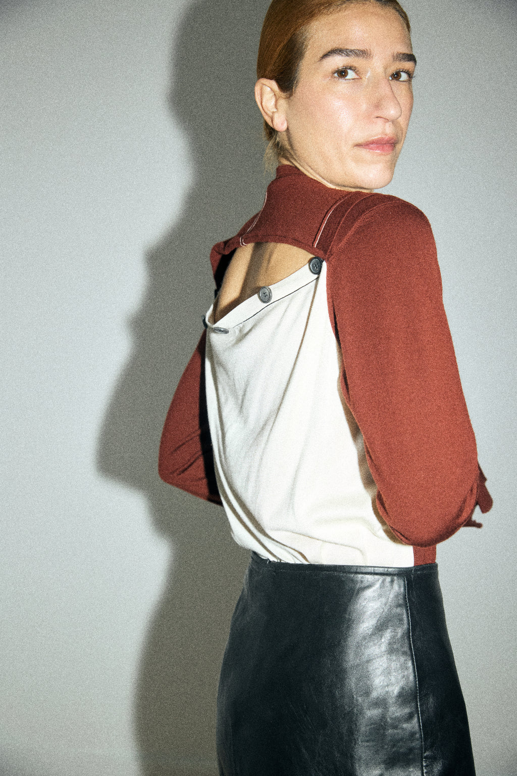 Person wearing a red jacket over a white shirt with a black leather skirt on a plain background
