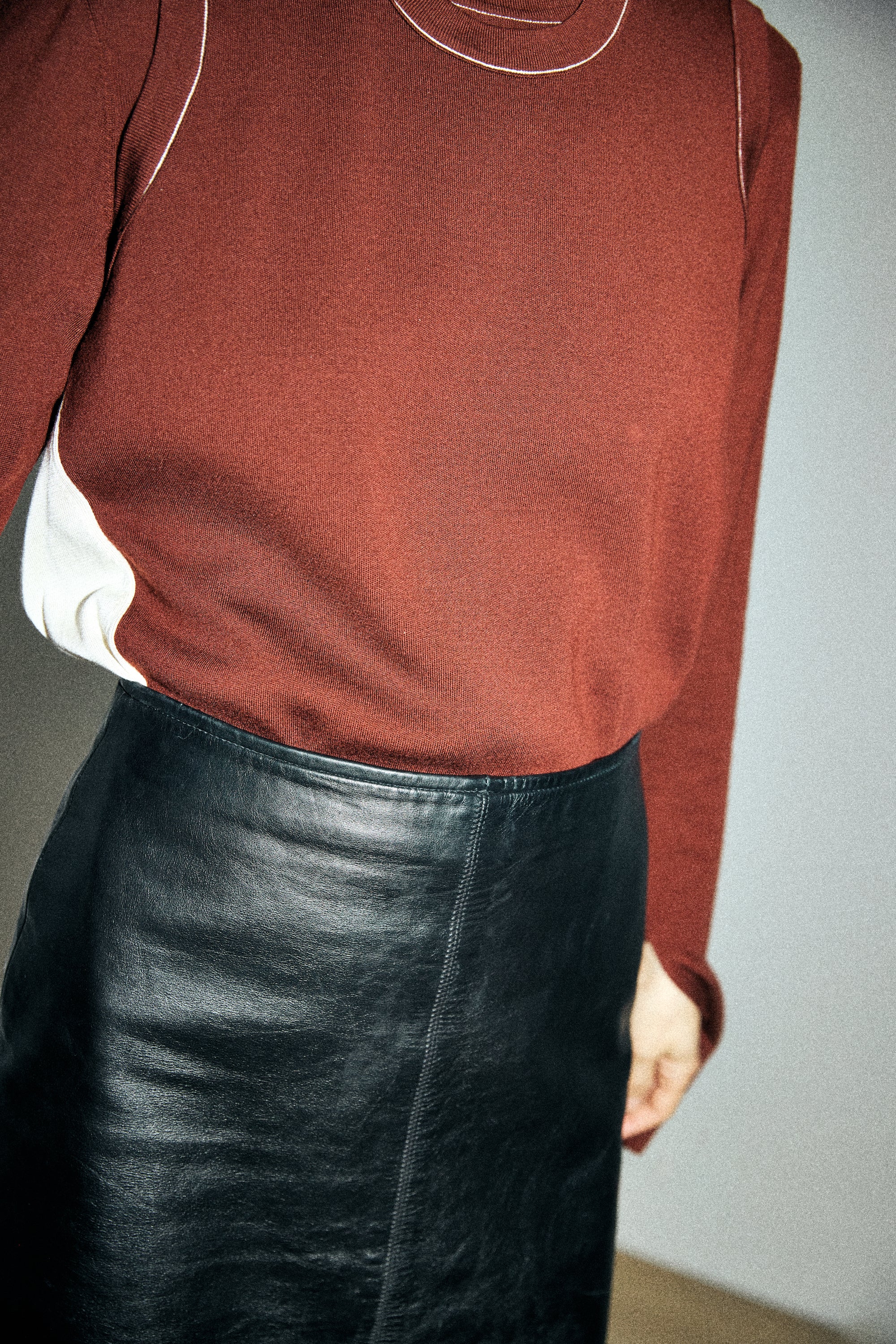 Person wearing a rust-colored sweater and black leather skirt against a plain background