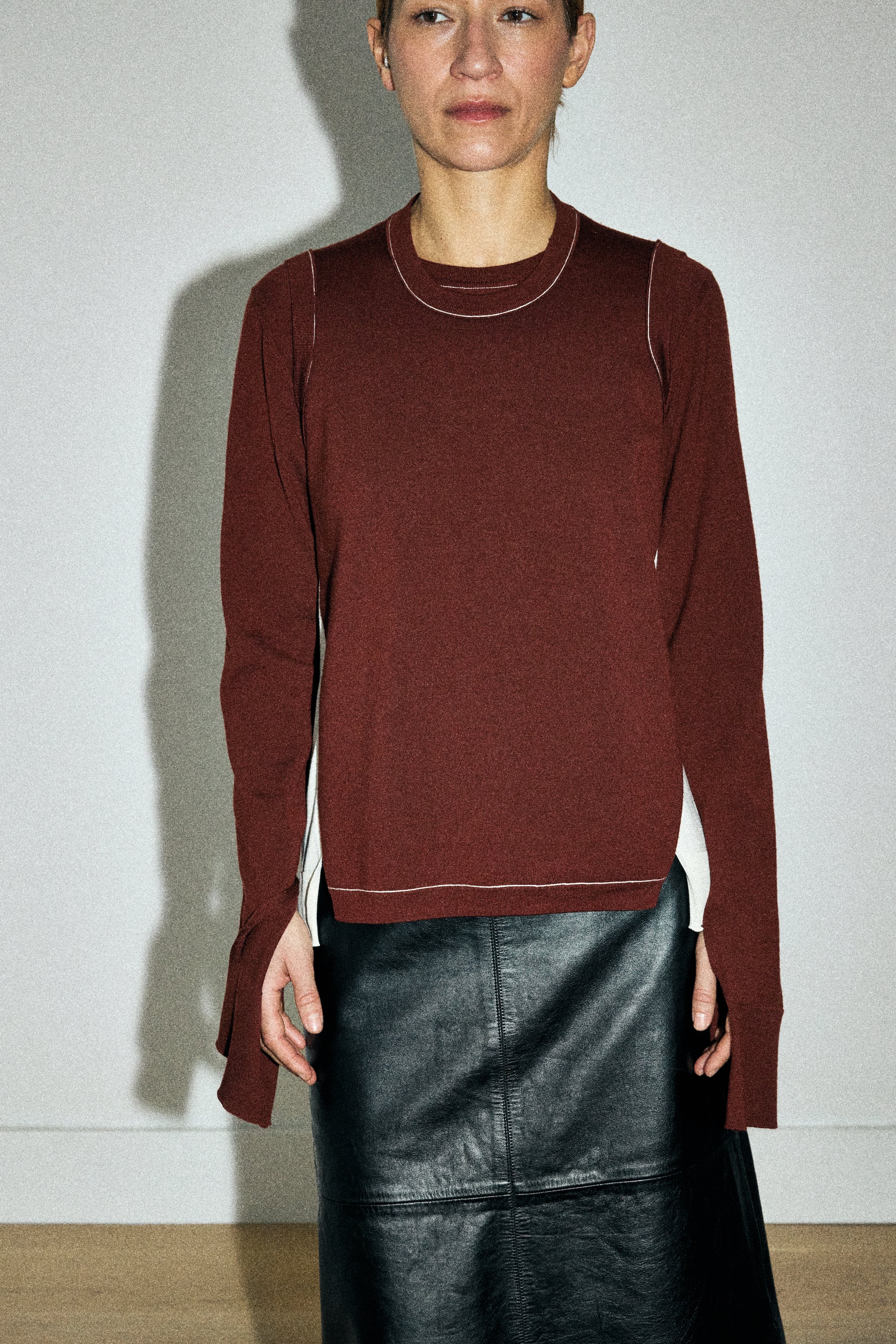 Person wearing a maroon sweater and black leather skirt against a plain background