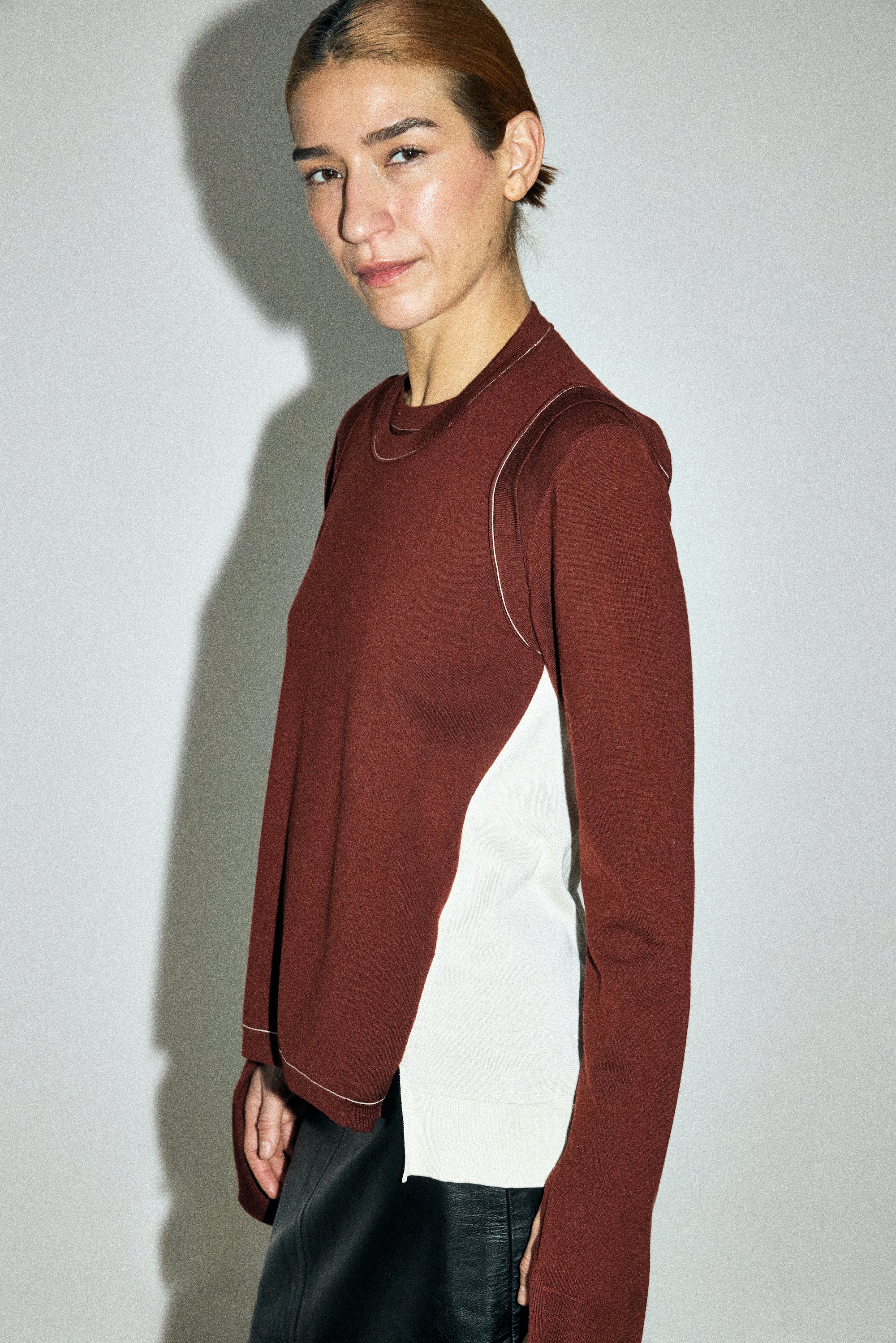 Person wearing a maroon long-sleeve top with white accents on a plain background