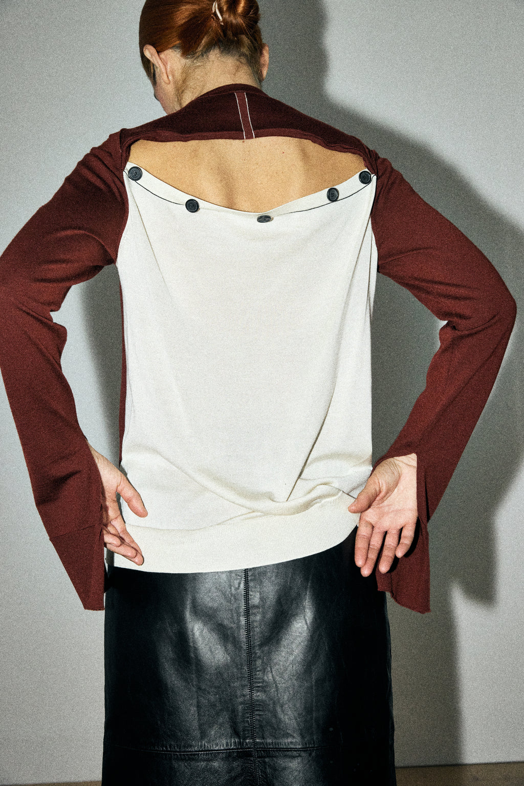 Person wearing a maroon cardigan over a white top with black buttons, standing against a plain background.