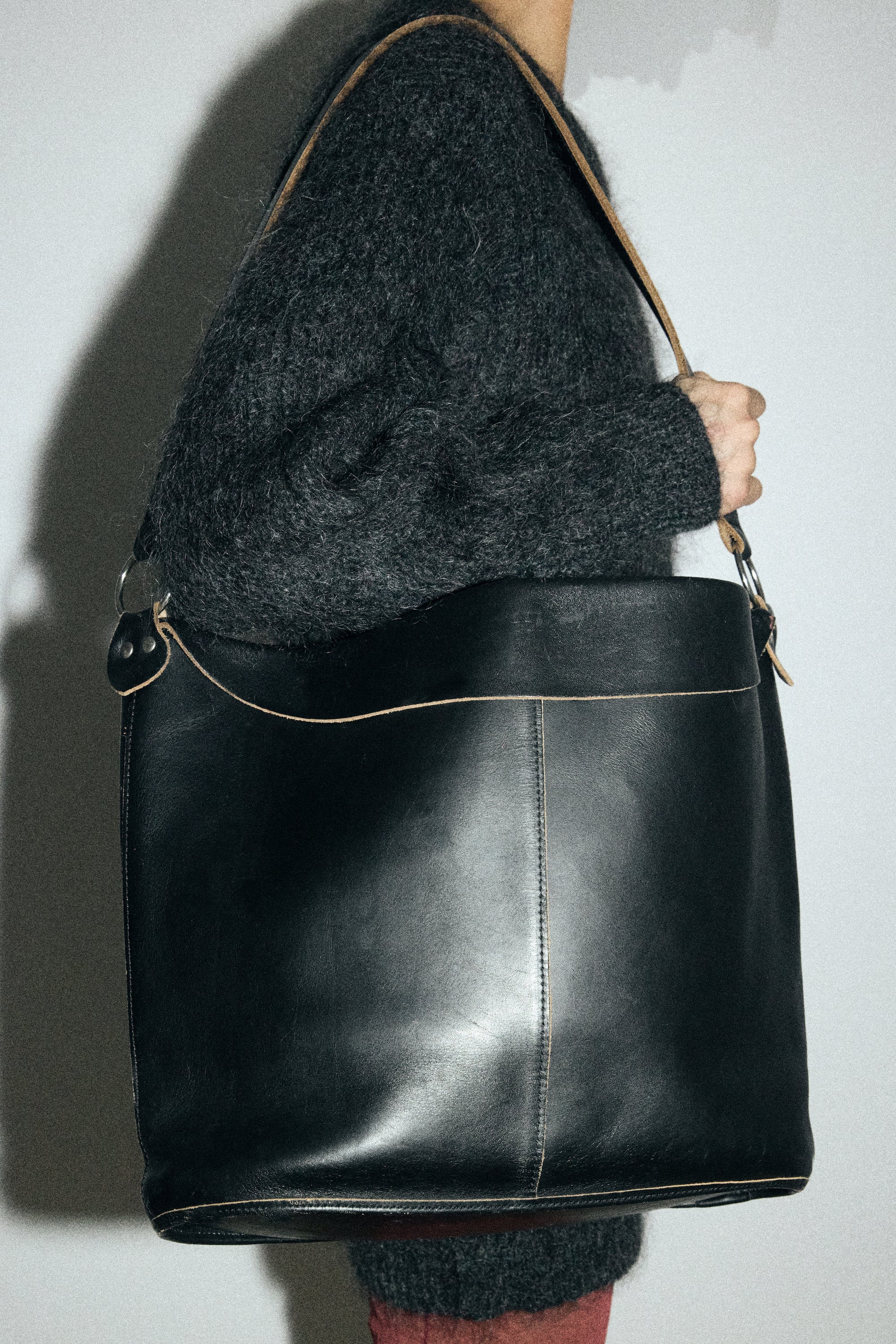 Person holding a black leather handbag against a plain background