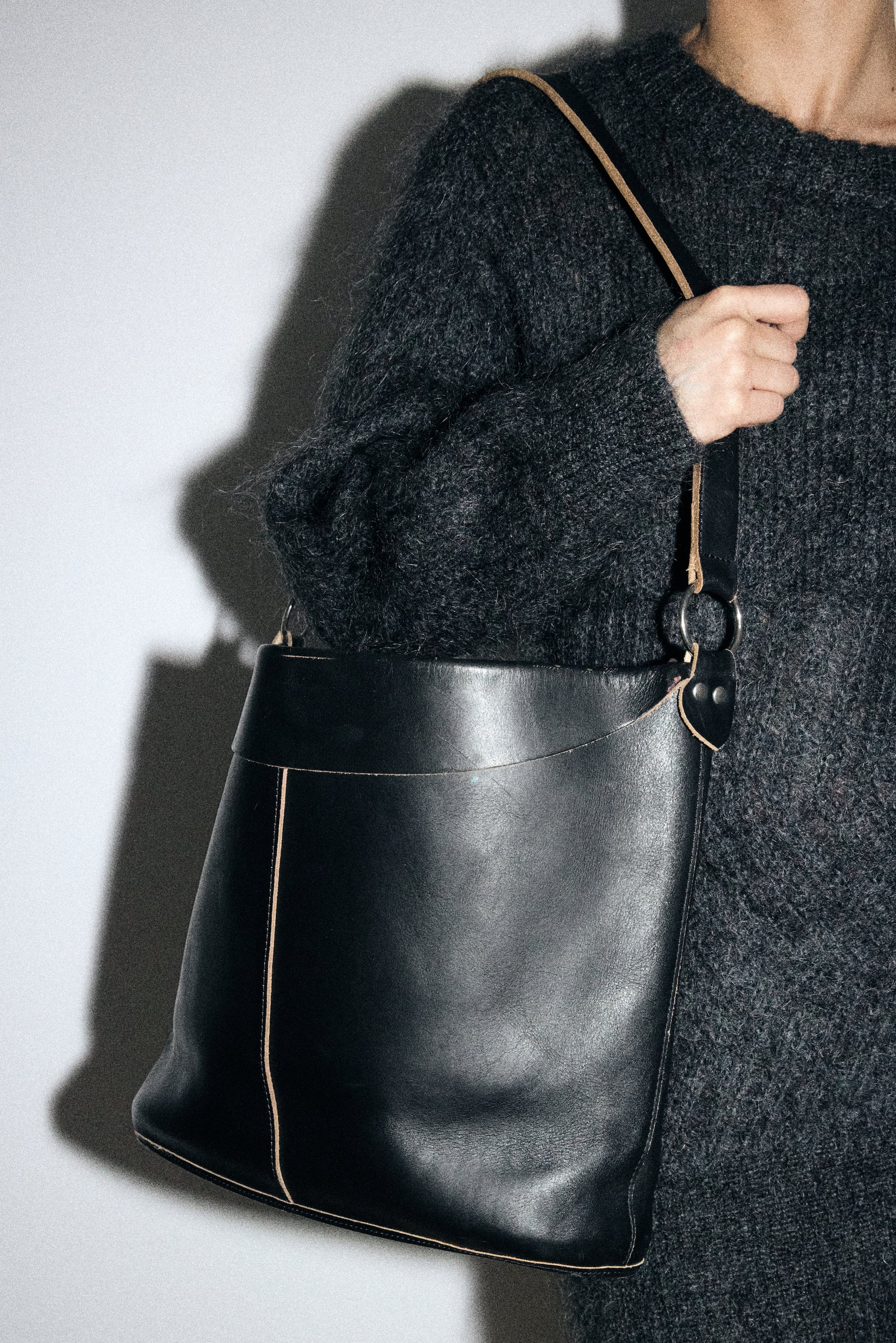 Person holding a black leather handbag against a plain background