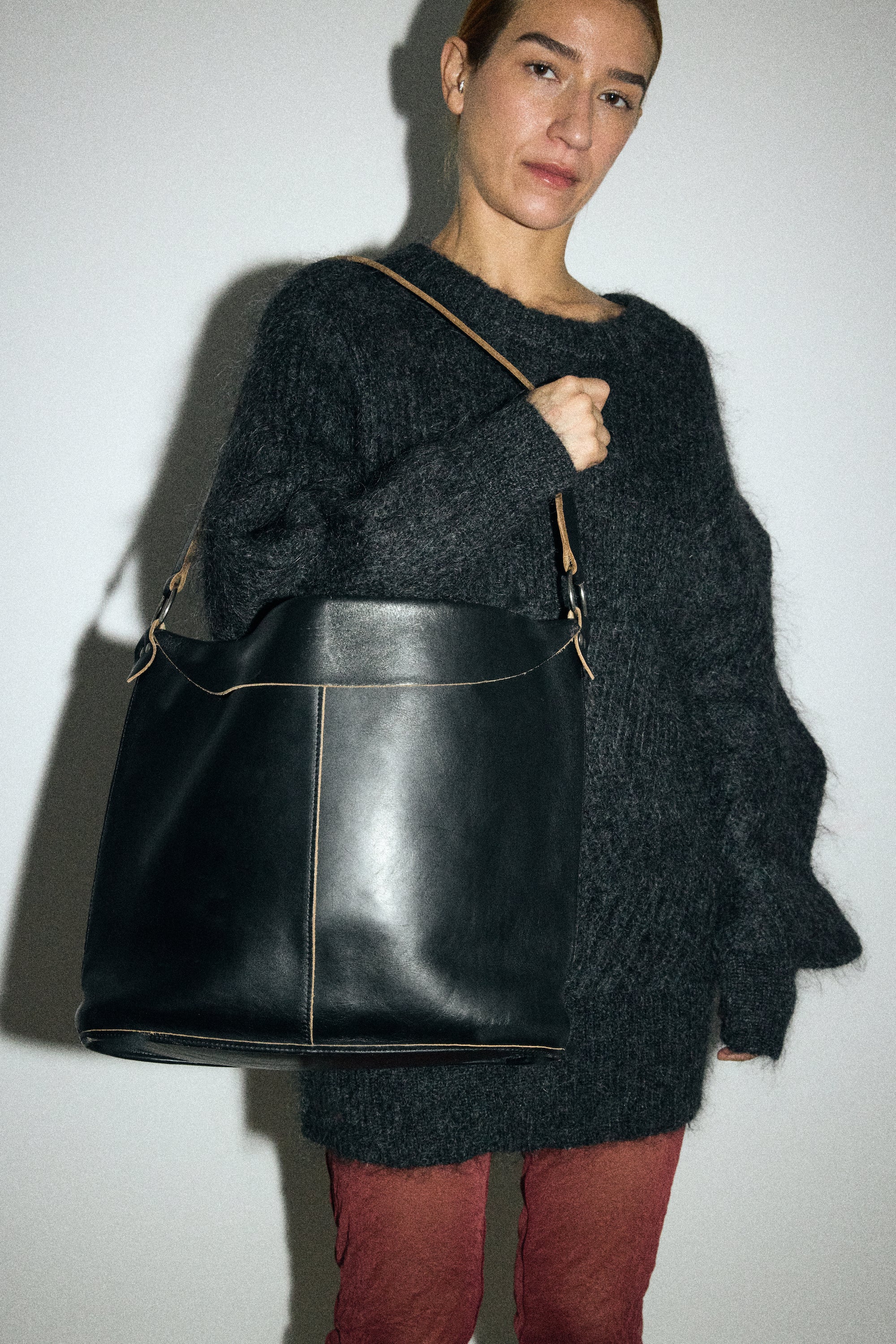 Person wearing a dark gray sweater and holding a black leather bag against a white background