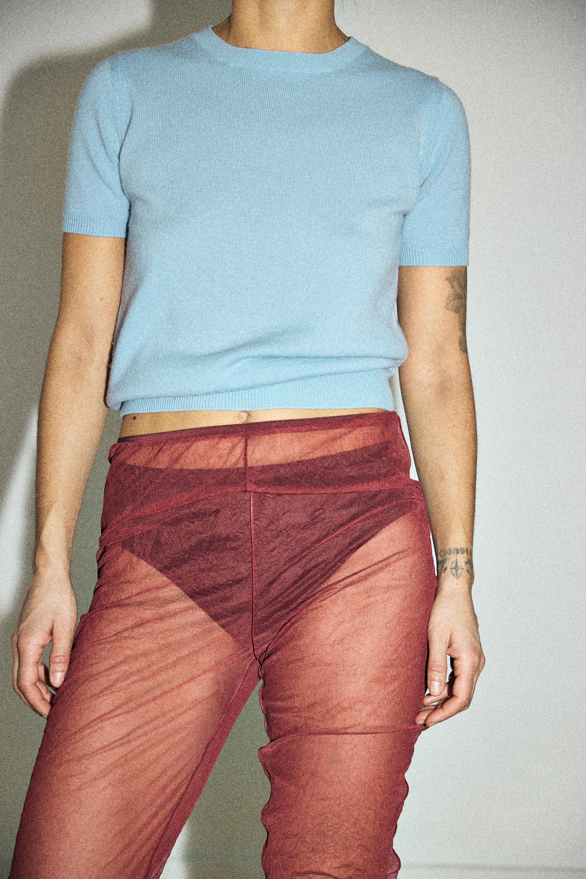 Person wearing a light blue t-shirt and red pants against a neutral background