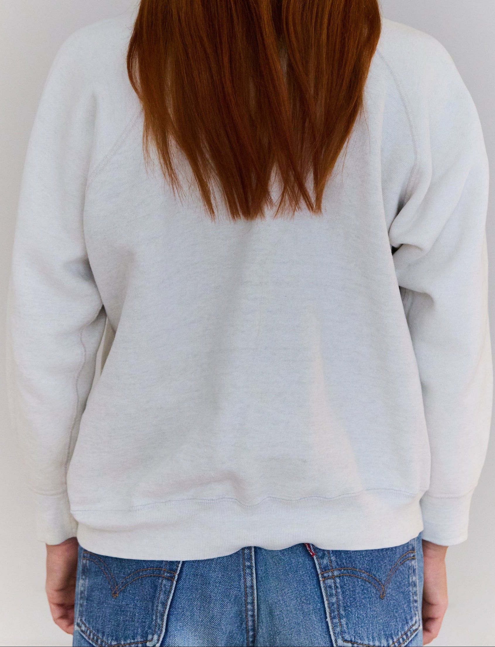 Person wearing a light gray sweatshirt and blue jeans against a white background