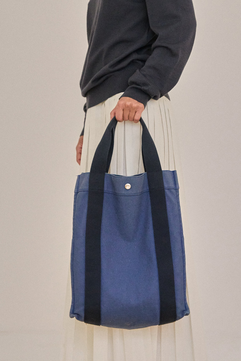 Person holding a blue and black tote bag against a neutral background