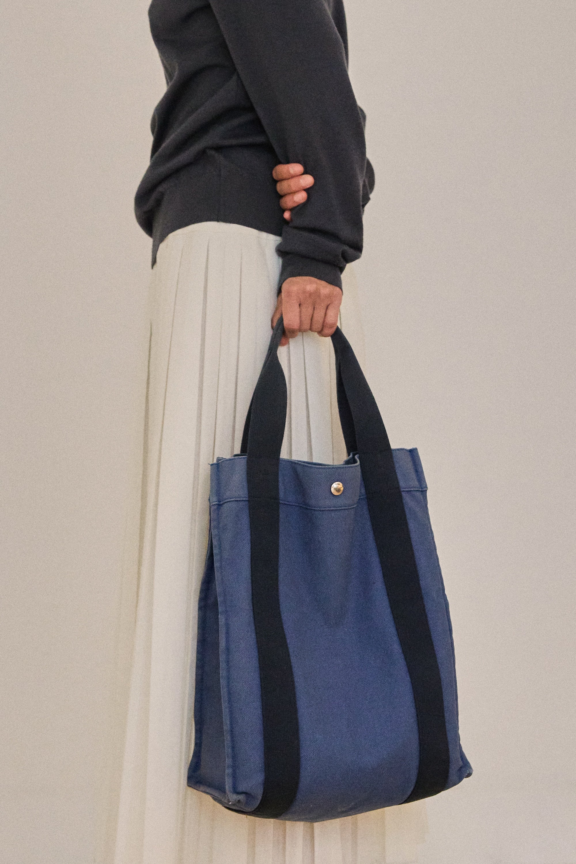 Person holding a blue tote bag with black straps against a neutral background