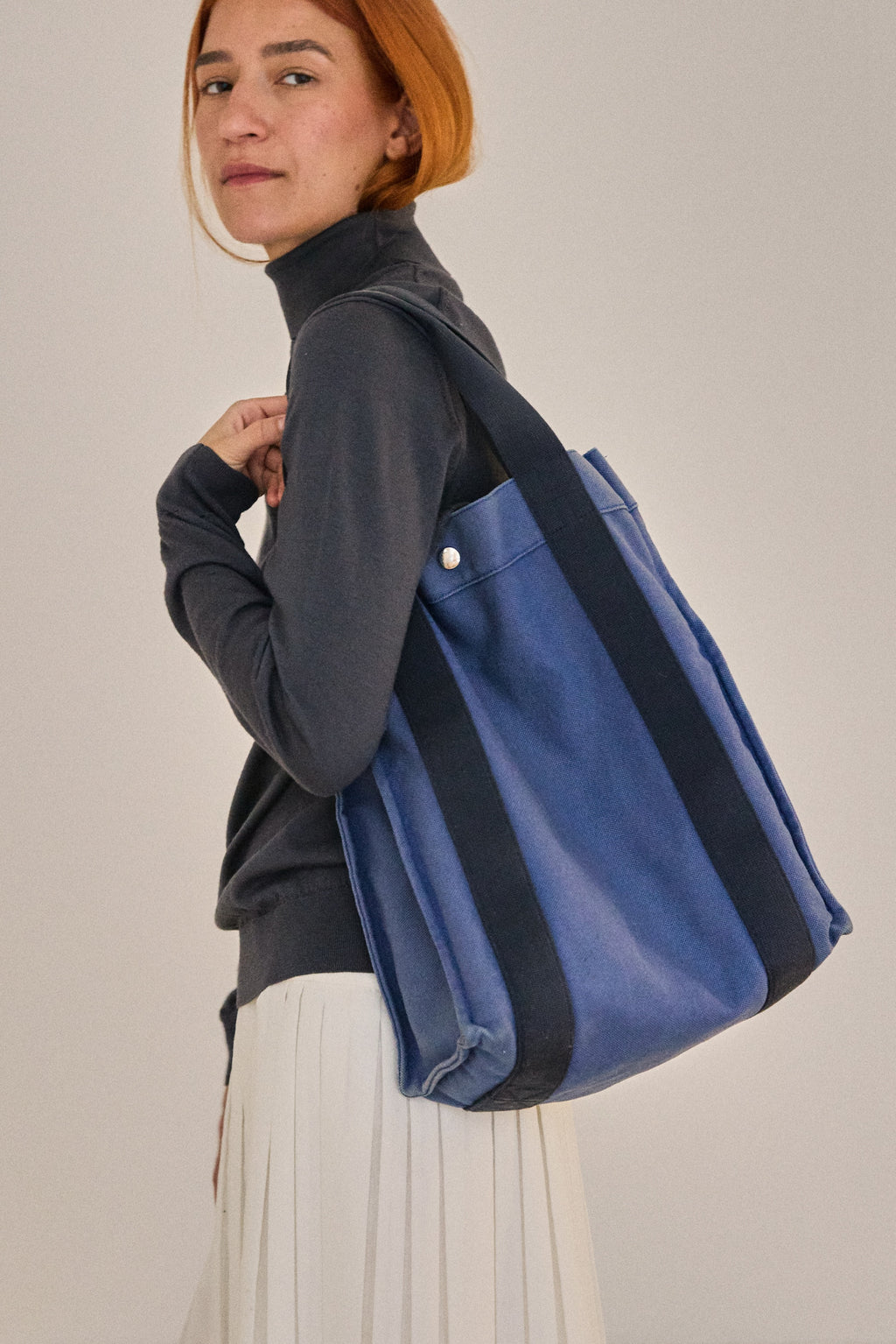 Person carrying a blue tote bag on a plain background