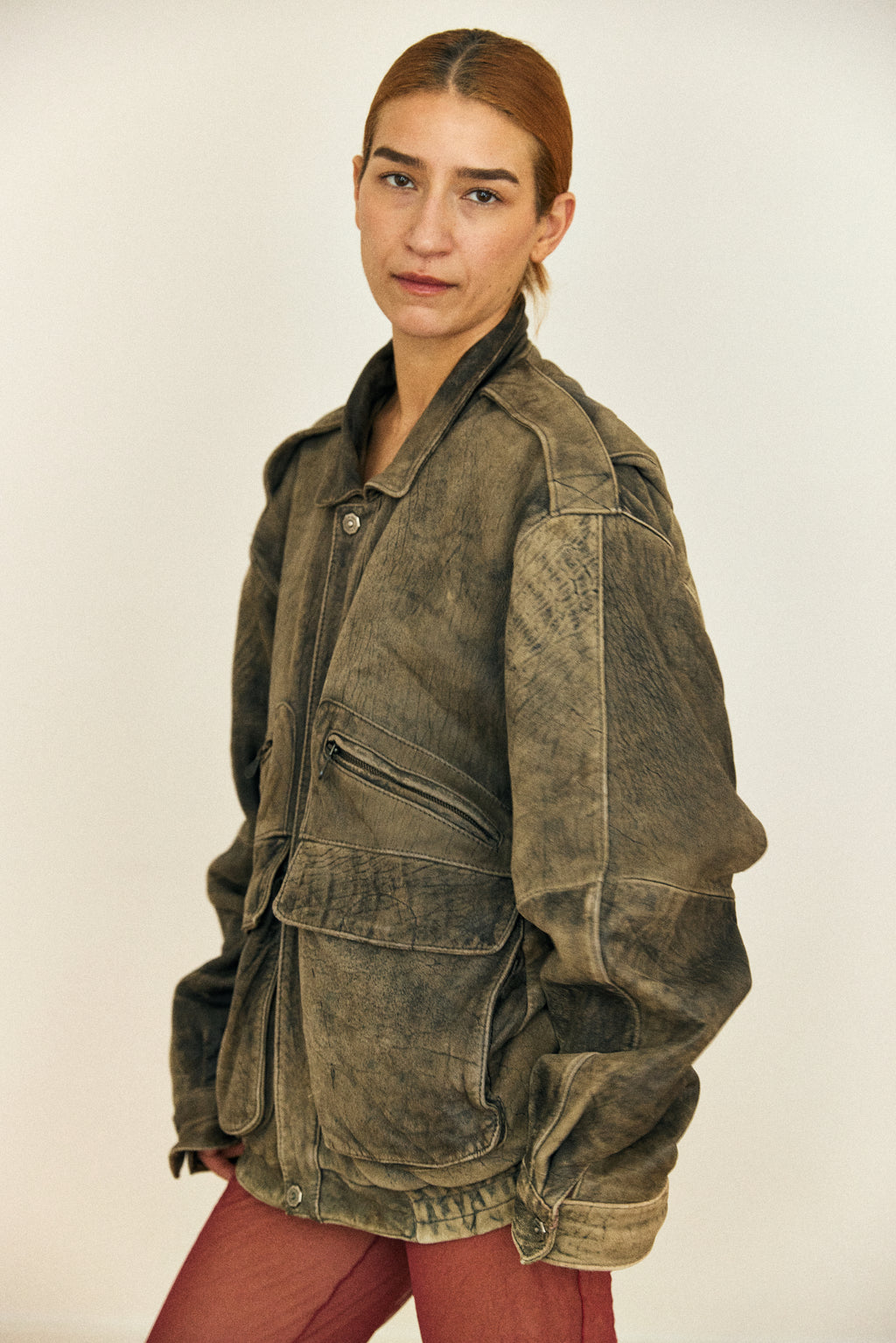 Person wearing a worn-out green jacket against a plain background