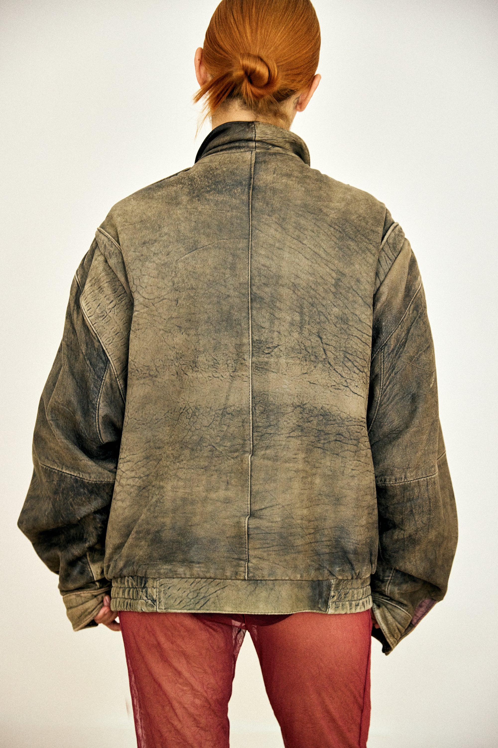 Person wearing a worn-out denim jacket and red pants on a plain background