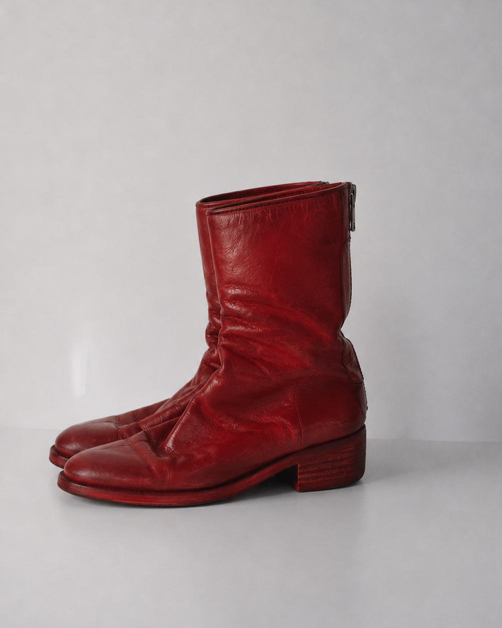 A pair of red leather ankle boots with a slouchy shaft and low block heel, photographed against a neutral light gray background.