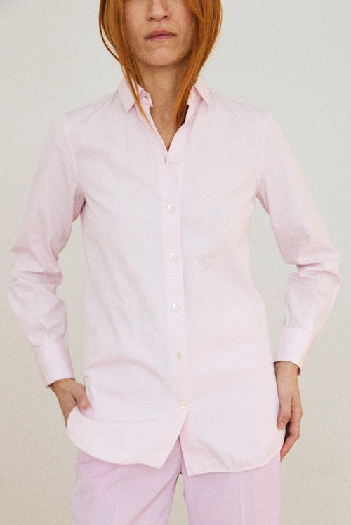 Person wearing a light pink shirt and pants against a plain background